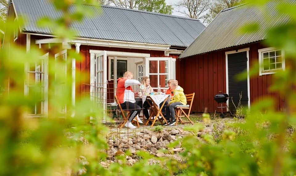 En grupp människor som sitter vid ett bord utanför ett rött hus.