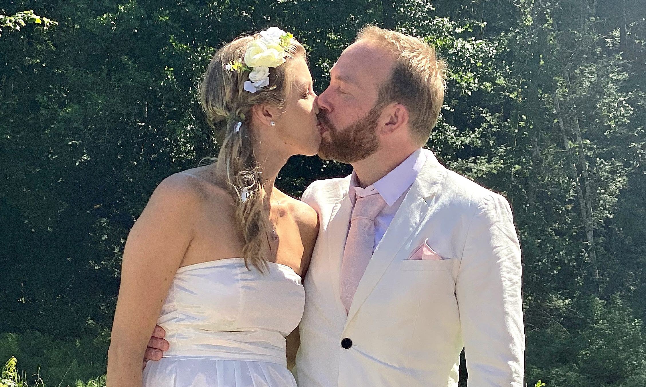 A bride and groom kissing in front of a table with wedding cakes set in the garden of Rydal Manor