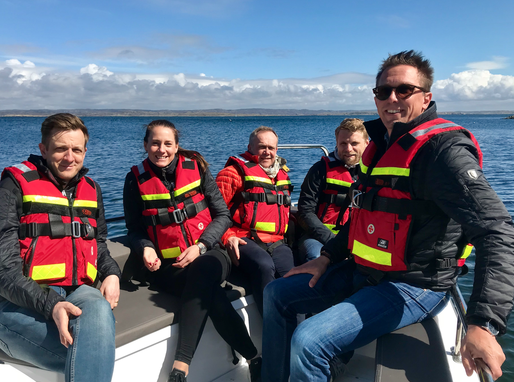Five persons wearing life wests sitting in a boat.