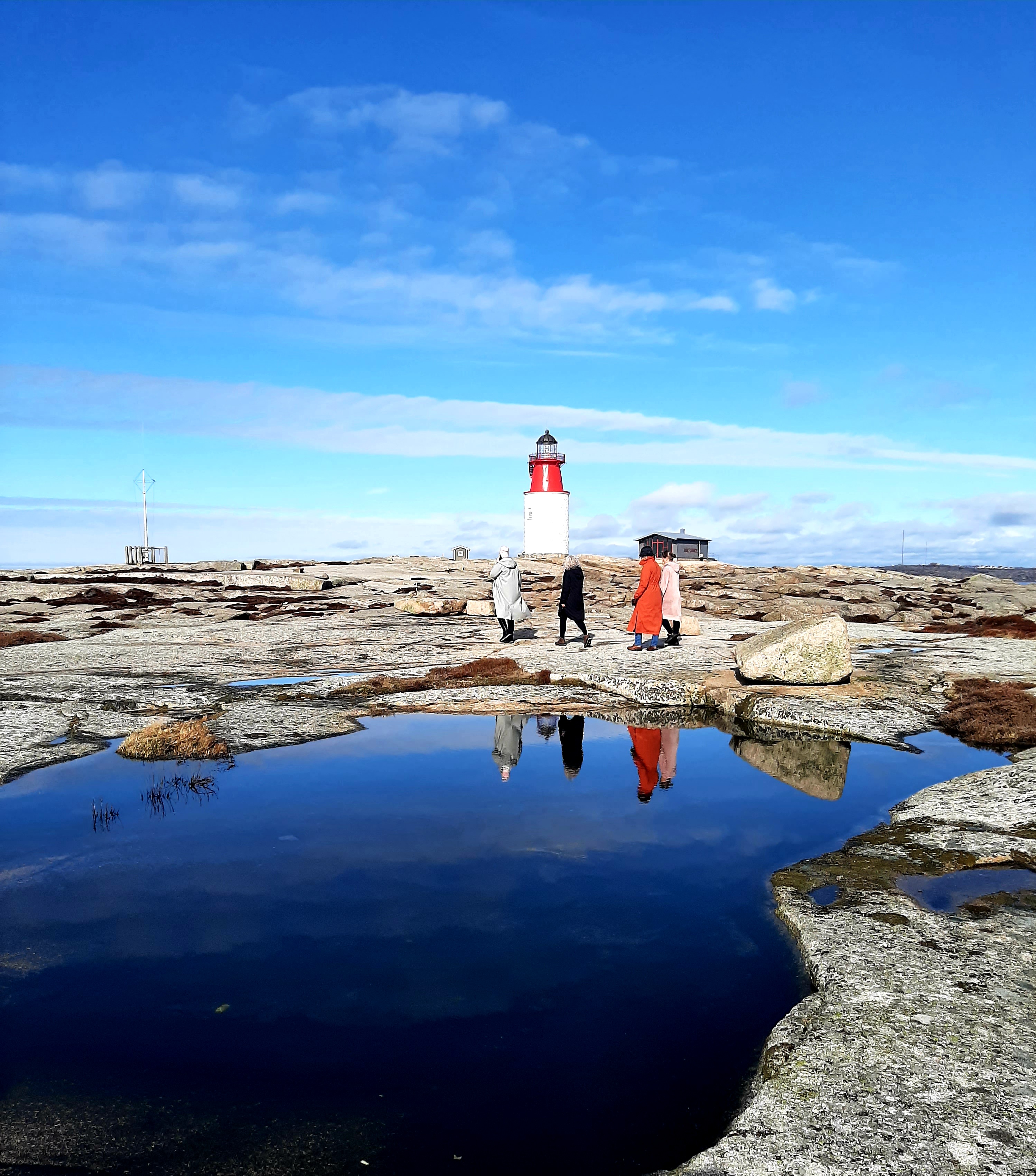 Guests walking on the rocks with the lighthouse in the background at Utpost Hållö