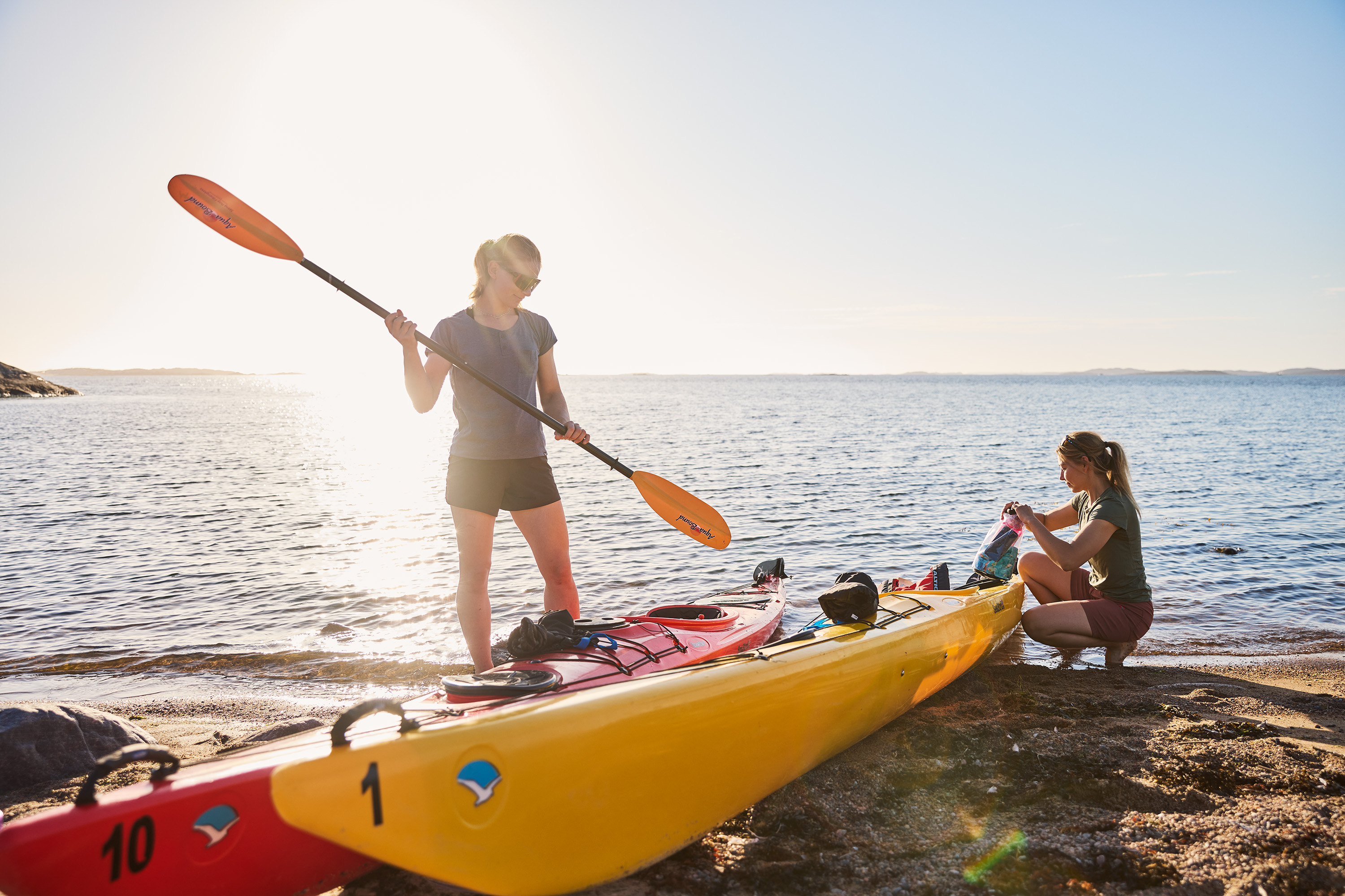 Two women on the beach by their kayaks.