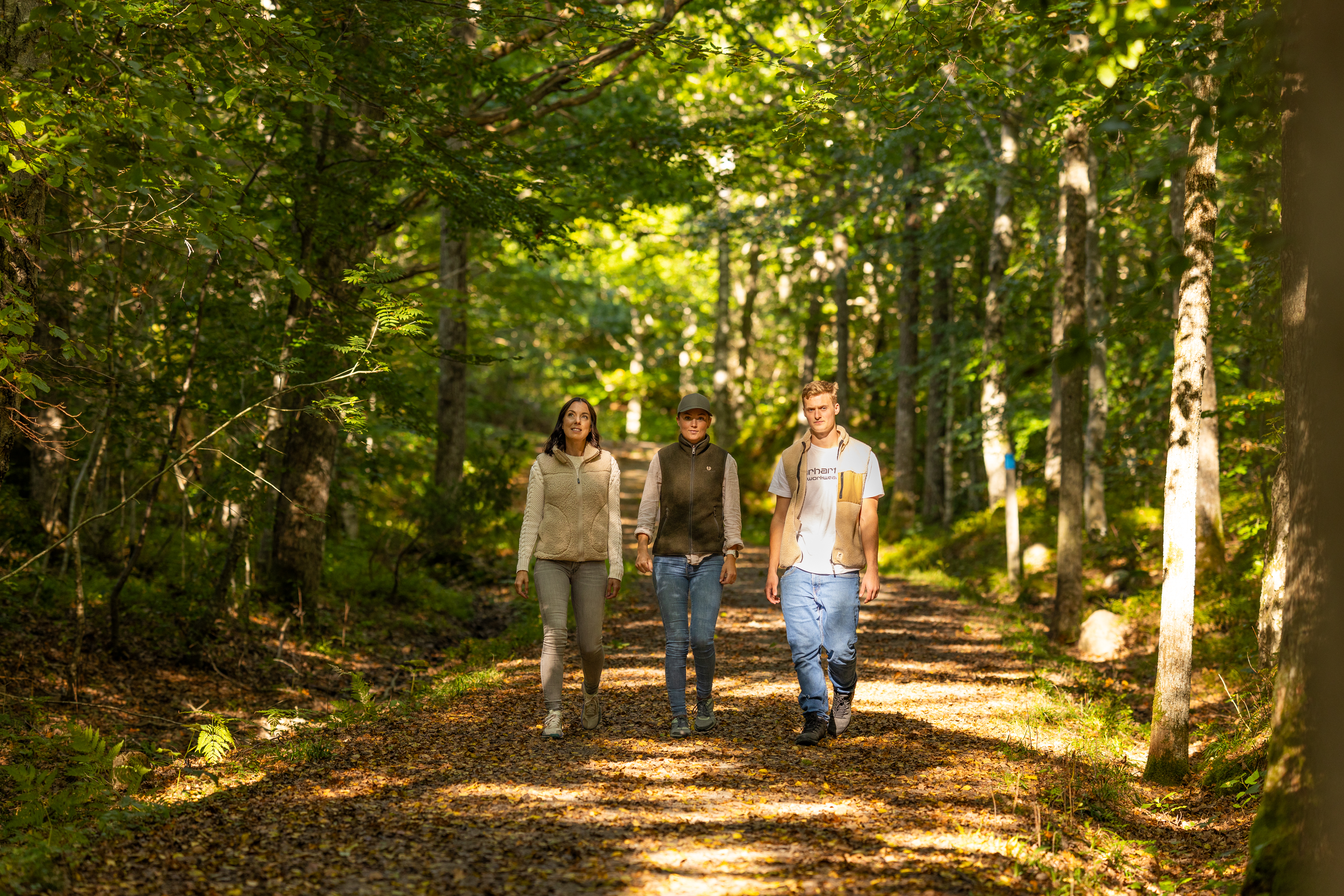 Three people are walking on a gravel road.