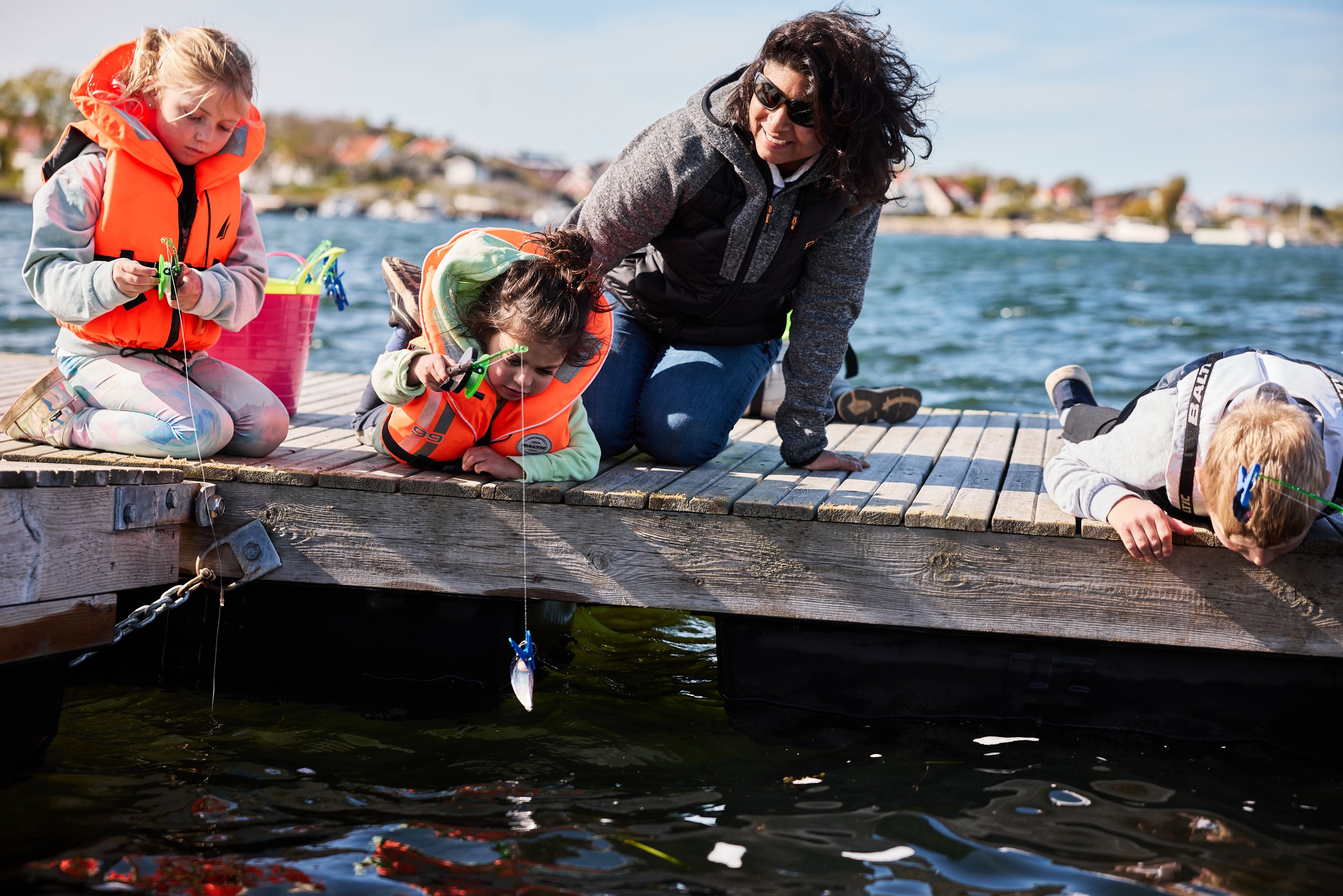 An adult and several children are crabbing from a pier using lines and buckets.