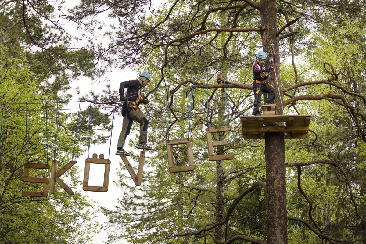 A man climbs a high-altitude track in a forest on letters that form the word Skövde.