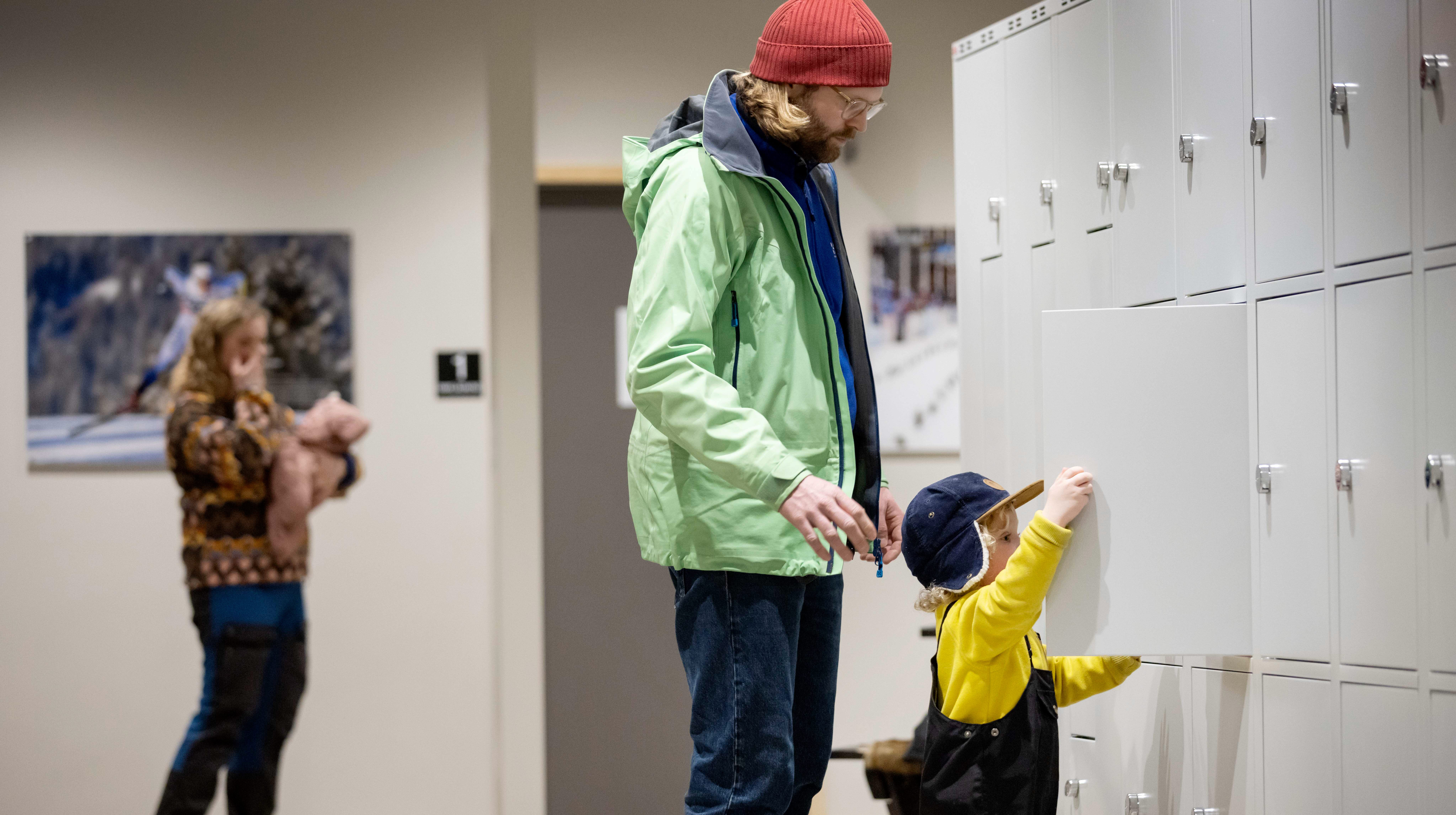 One wall is covered with storage cabinets. A small guy stands and closes one of the cupboards. Behind him is his father.