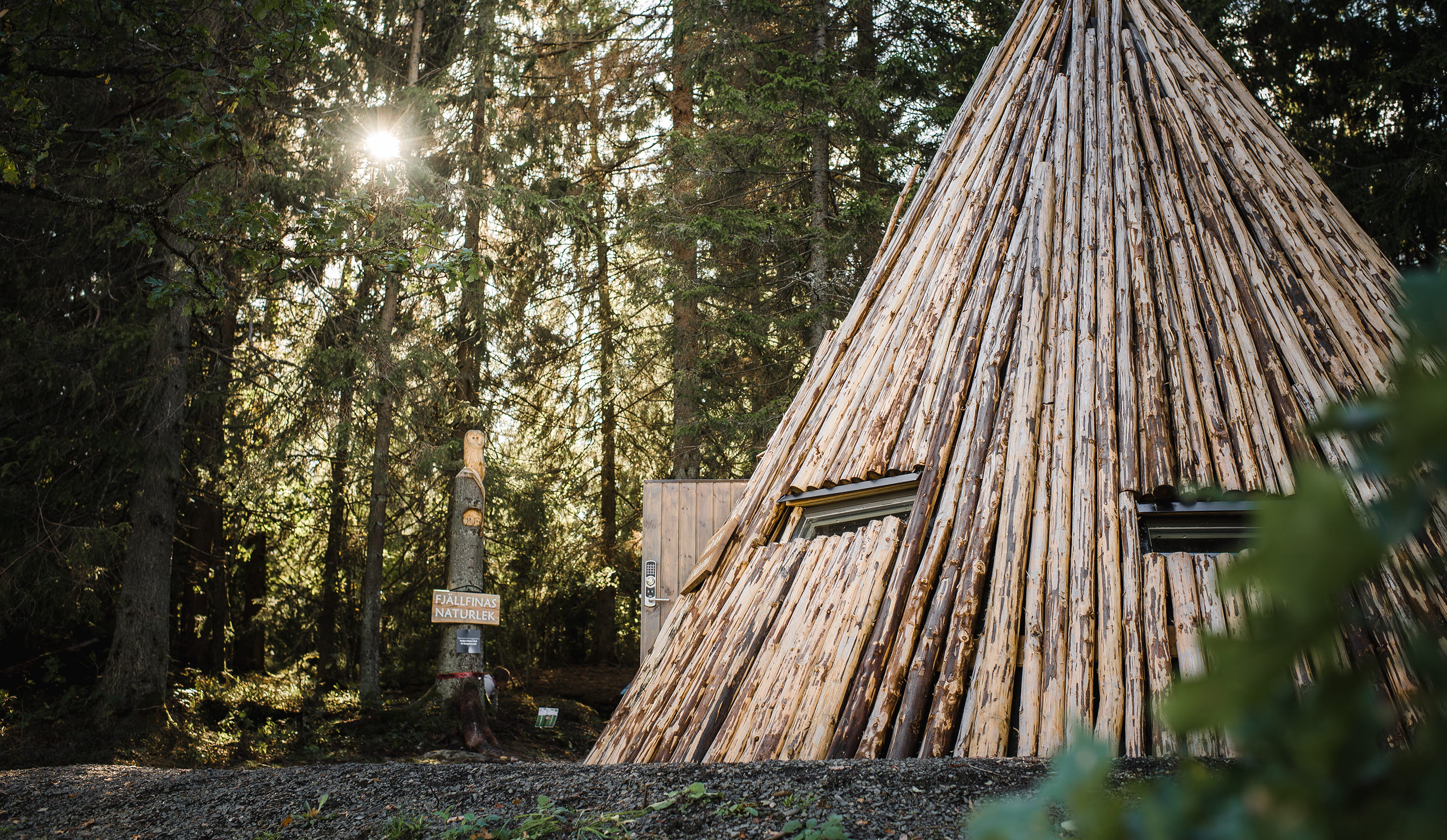 A large wooden hut in fine sunlight seeping in between the tree branches.