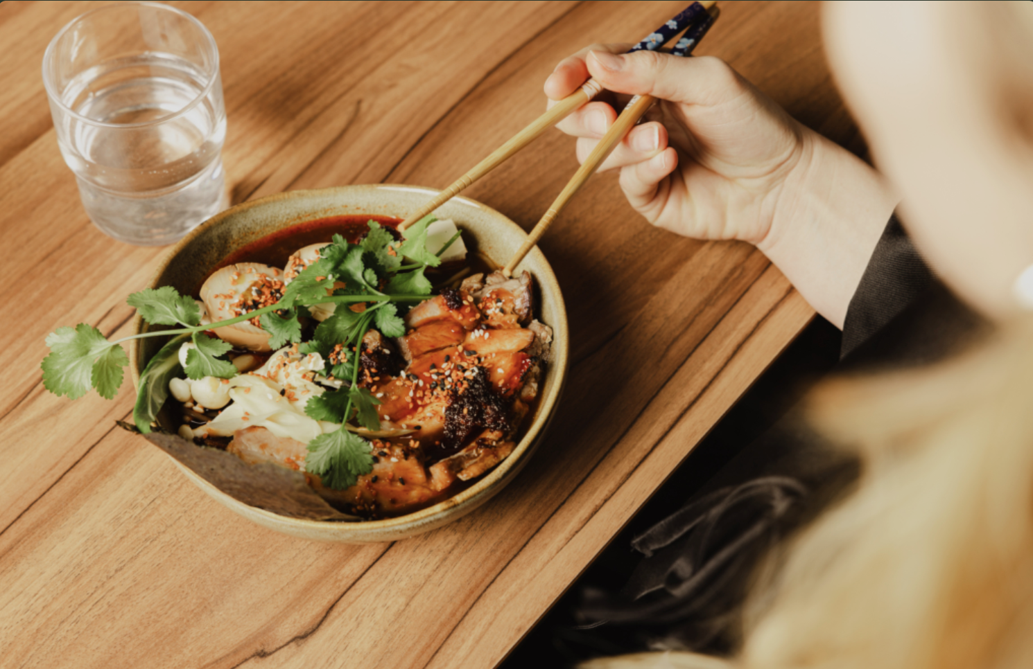 Plate of food on a wooden table, a hand holding chopsticks.