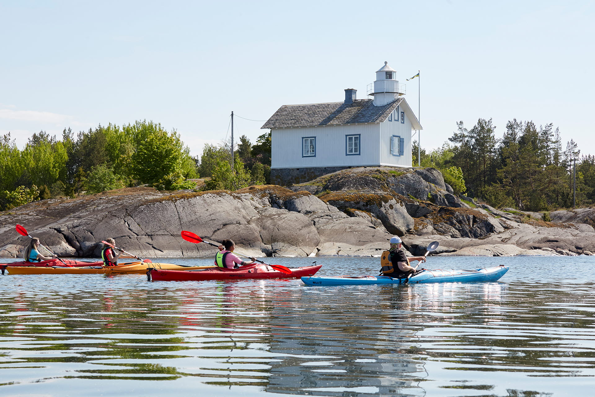 3 kayaks that are paddling in front of a white lighthouse.