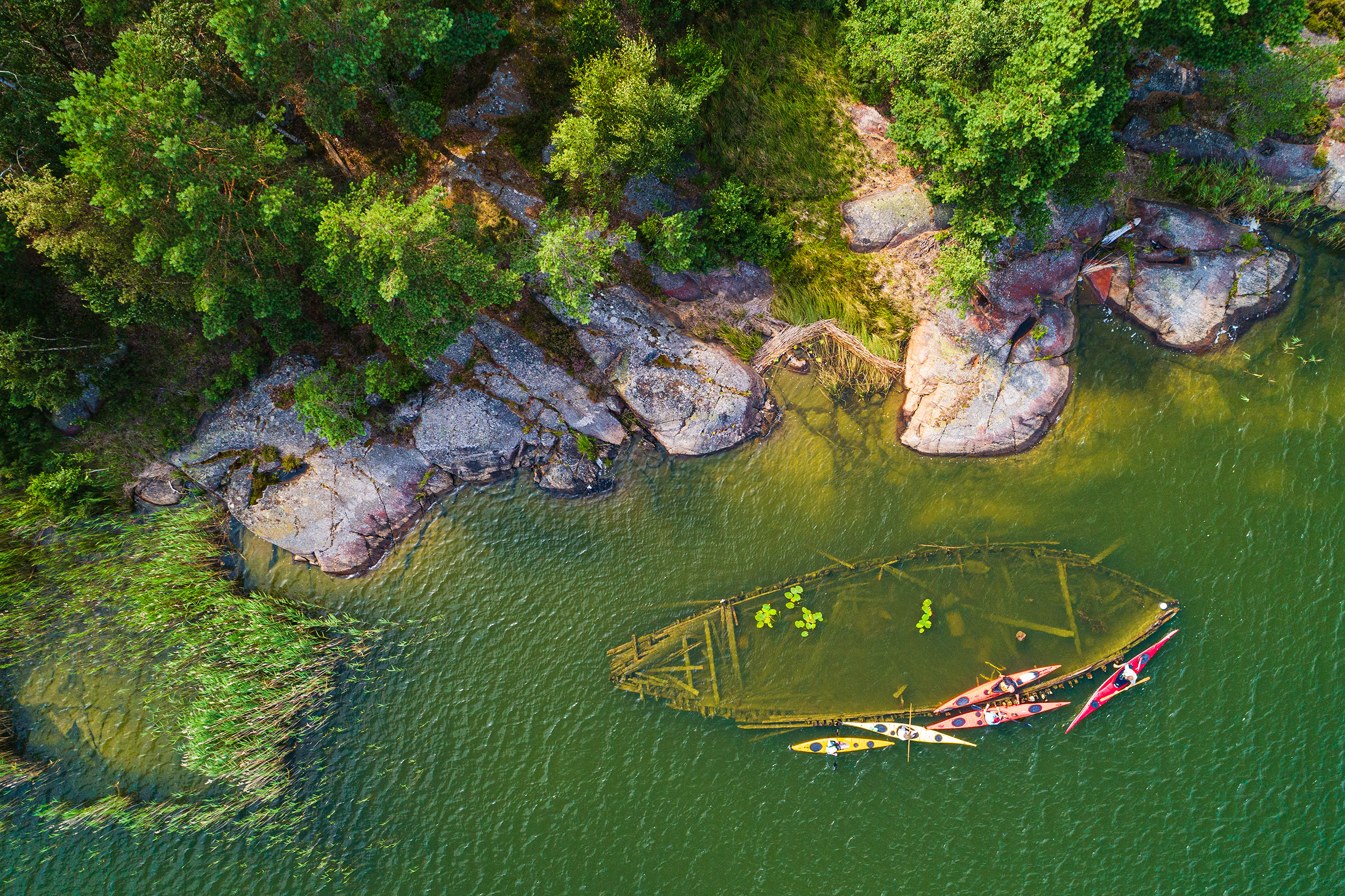 A wreck lying near land in the water. It can be seen from above.
