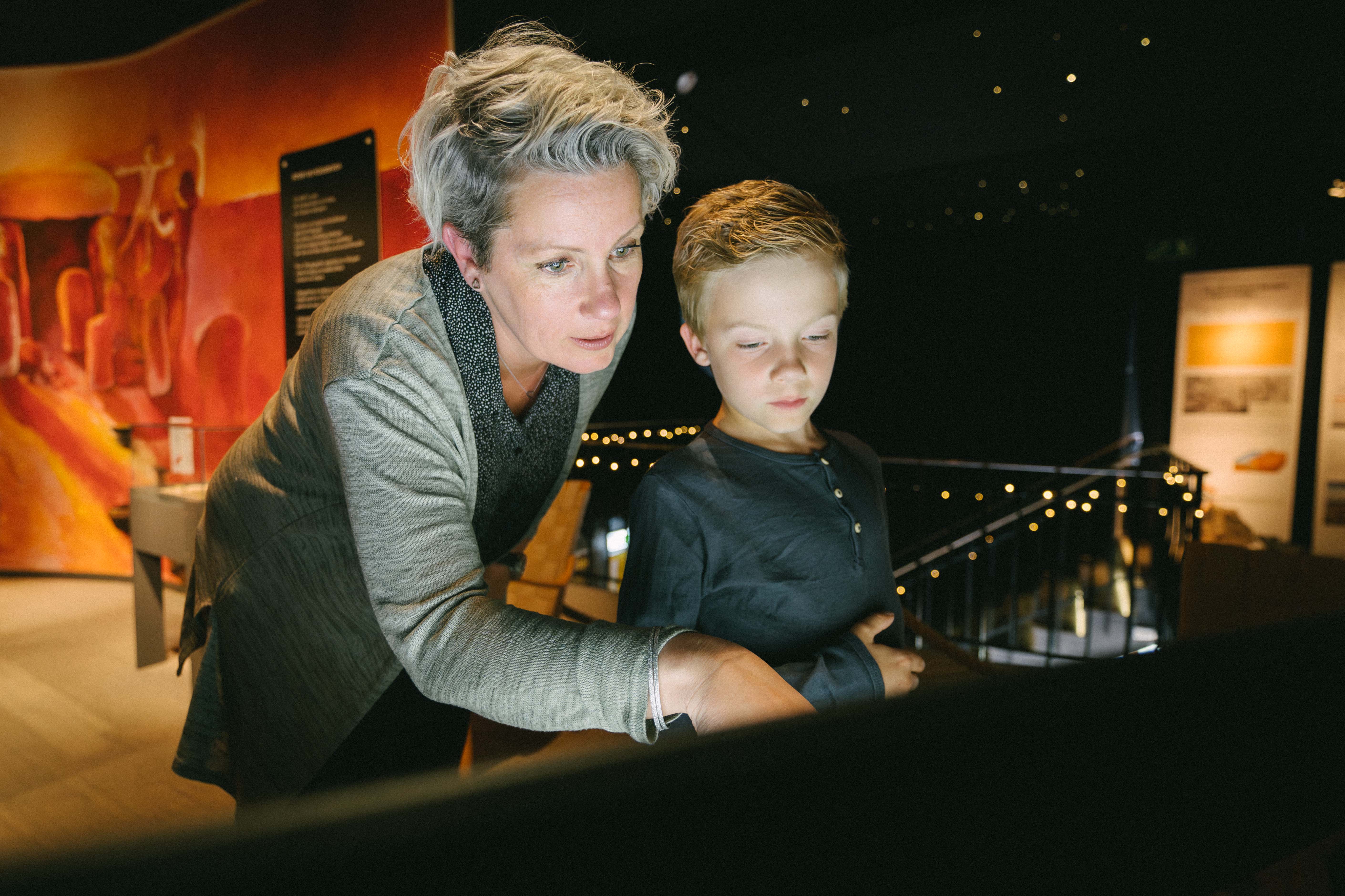 Vuxen och barn tittar tillsammans i forntidsutställningen på Falbygdens museum.