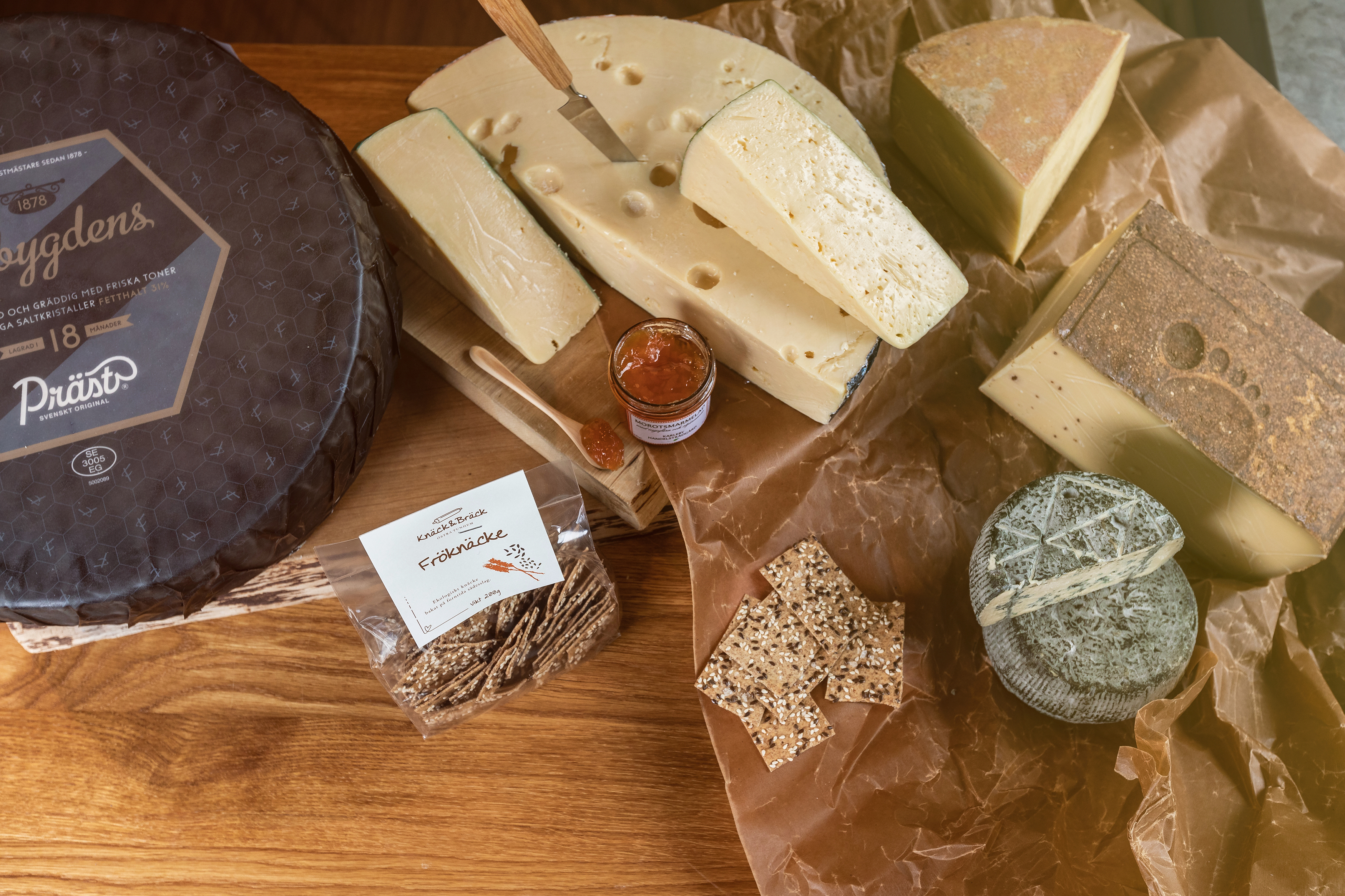 Different kinds of cheeses on a table. Also crispbread with seeds and a whole cheese with black packaging where it says Falbygdens Osteria.