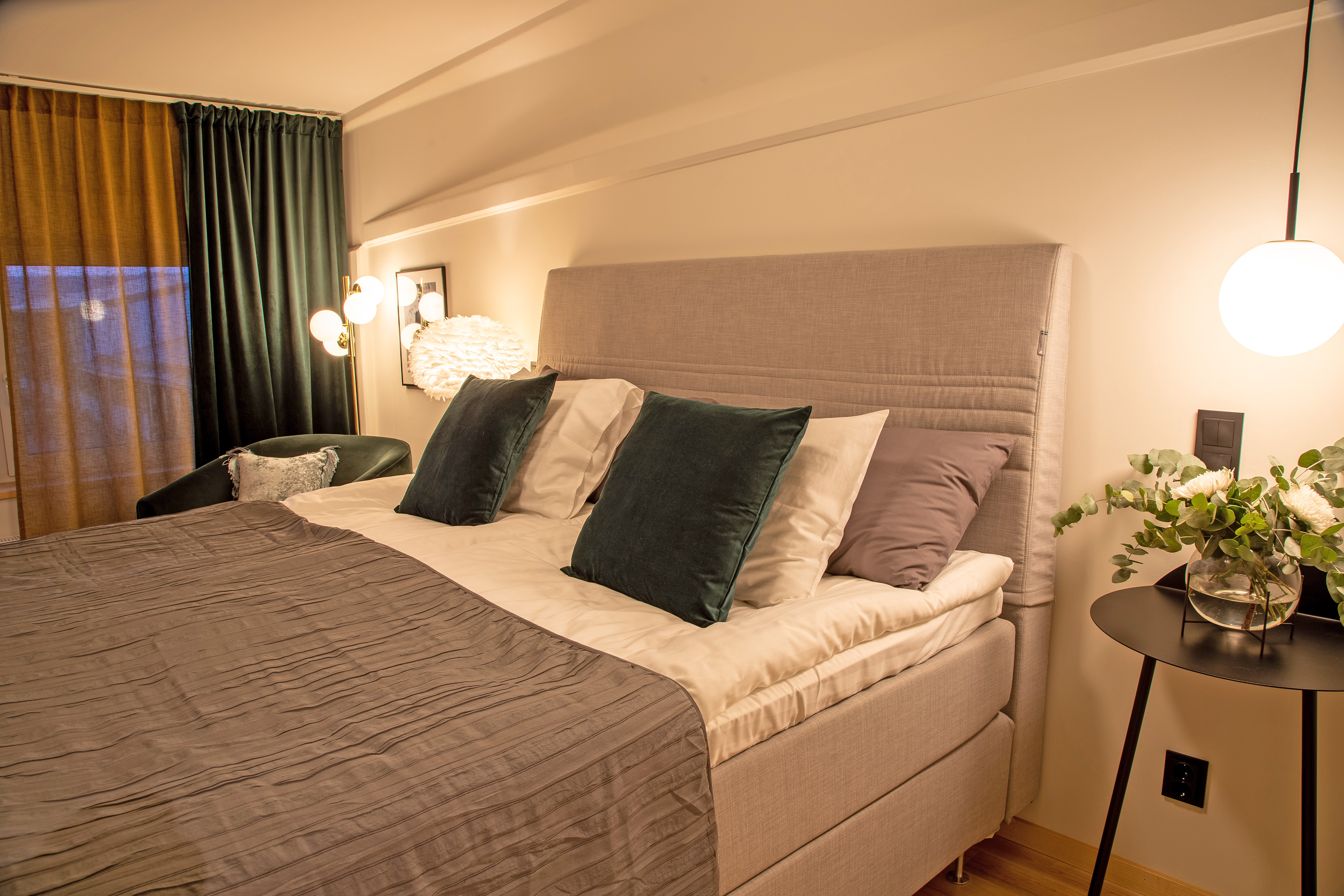 Bed with gray fabric, green curtains and pillows.