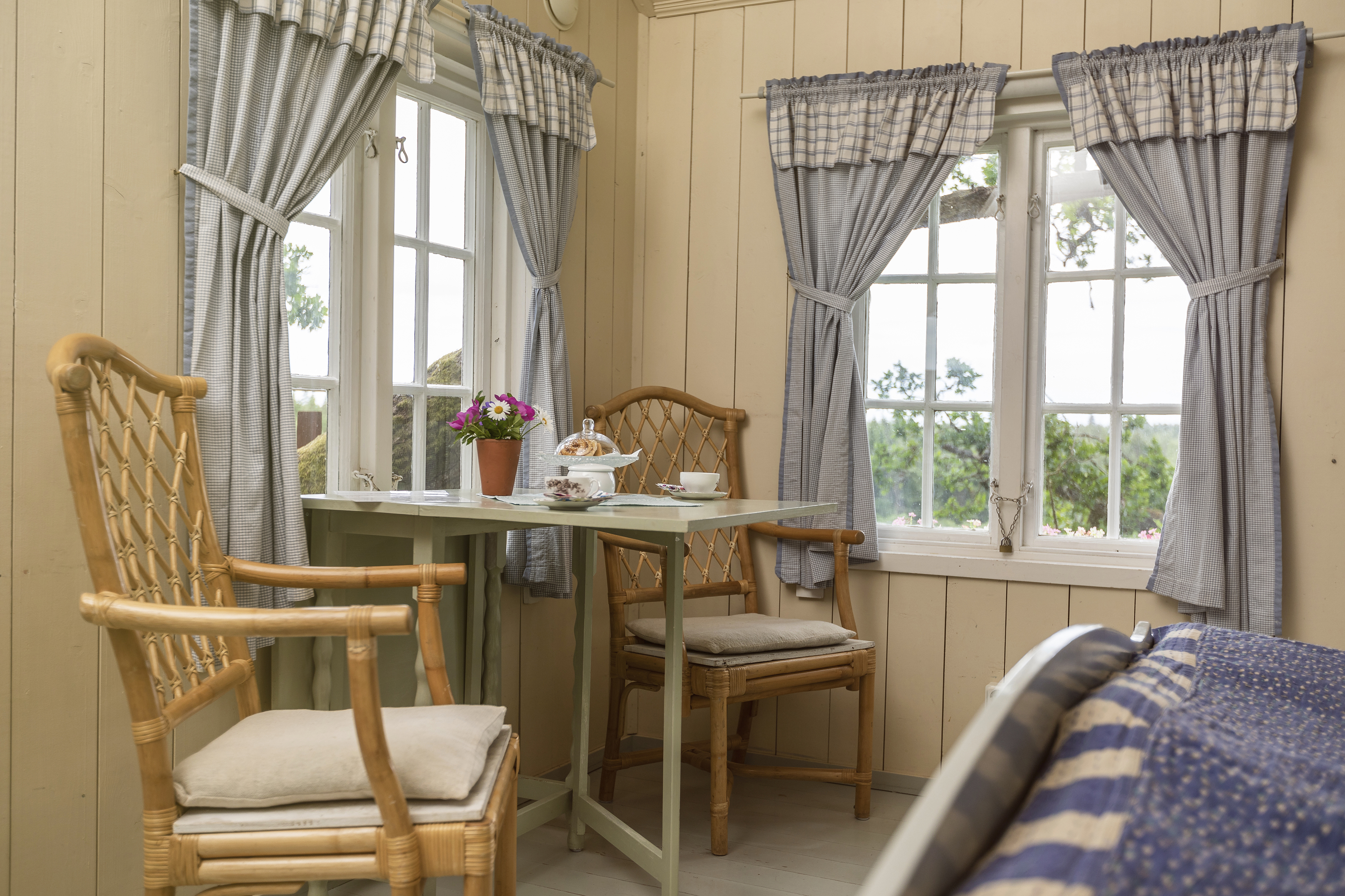 Small room with wooden walls, two windows with blue curtains, table and chairs.