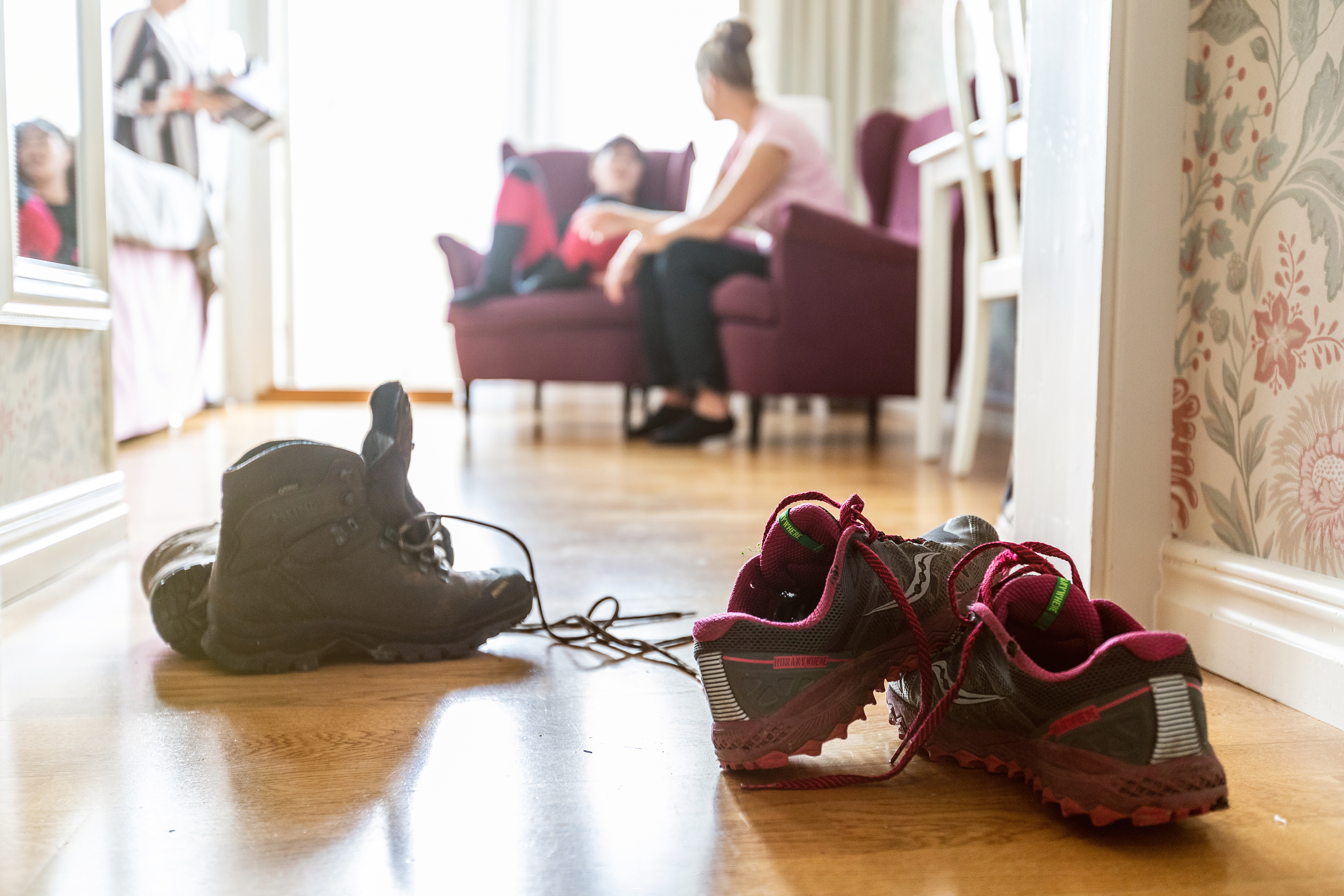 Two hiking boots are on the floor and two people are sitting in armchairs in the background.