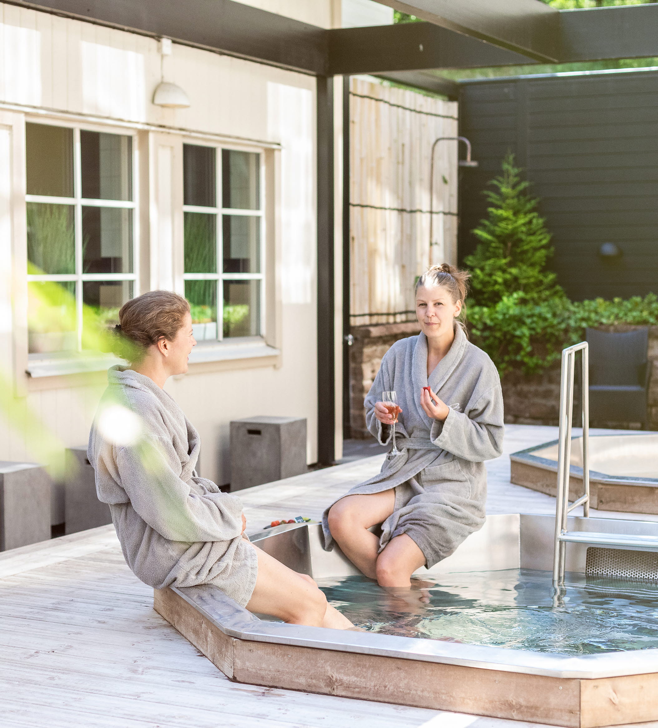 Two women sitting with bathrobes by an outdoor pool.