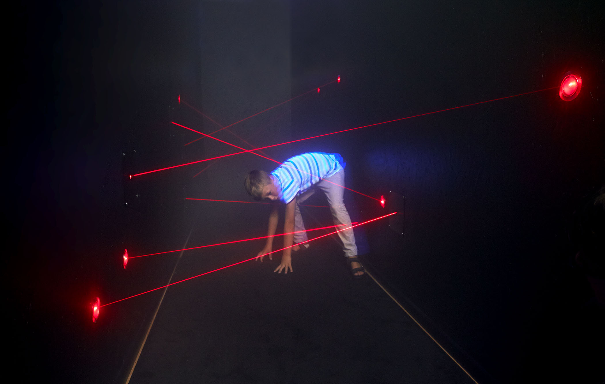 A child walking in a laser path with red rays in a dark room.