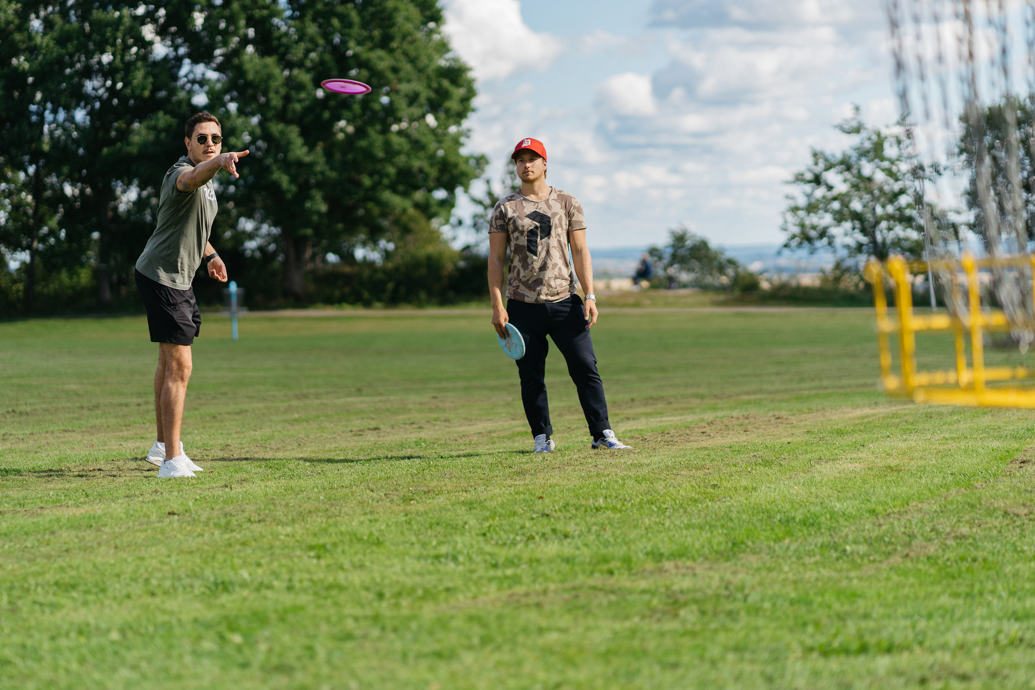 Two guys throwing a frisbee at a yellow metal basket.