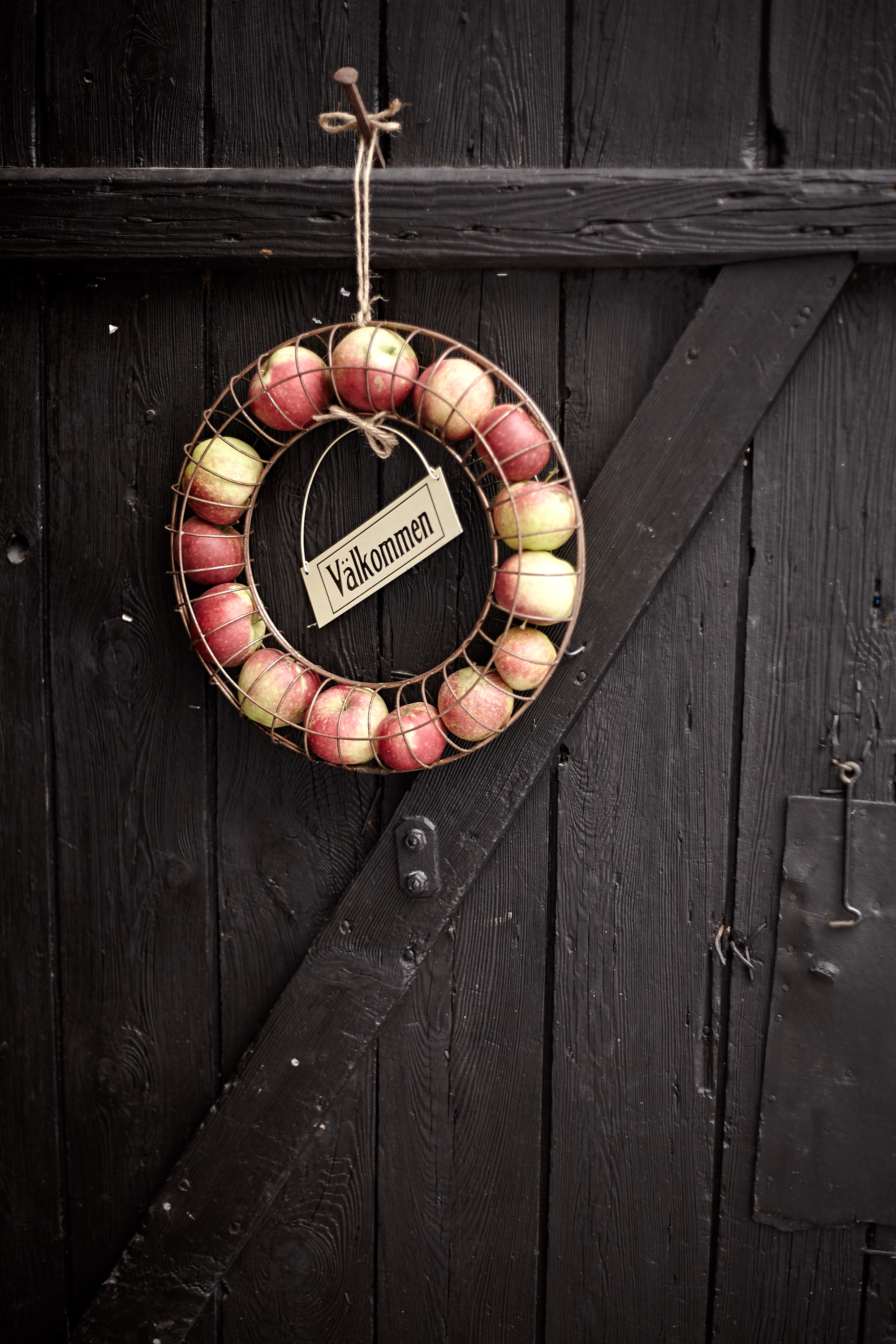 A black door with a wreath of apples, inside the wreath there is a sign with the text Welcome