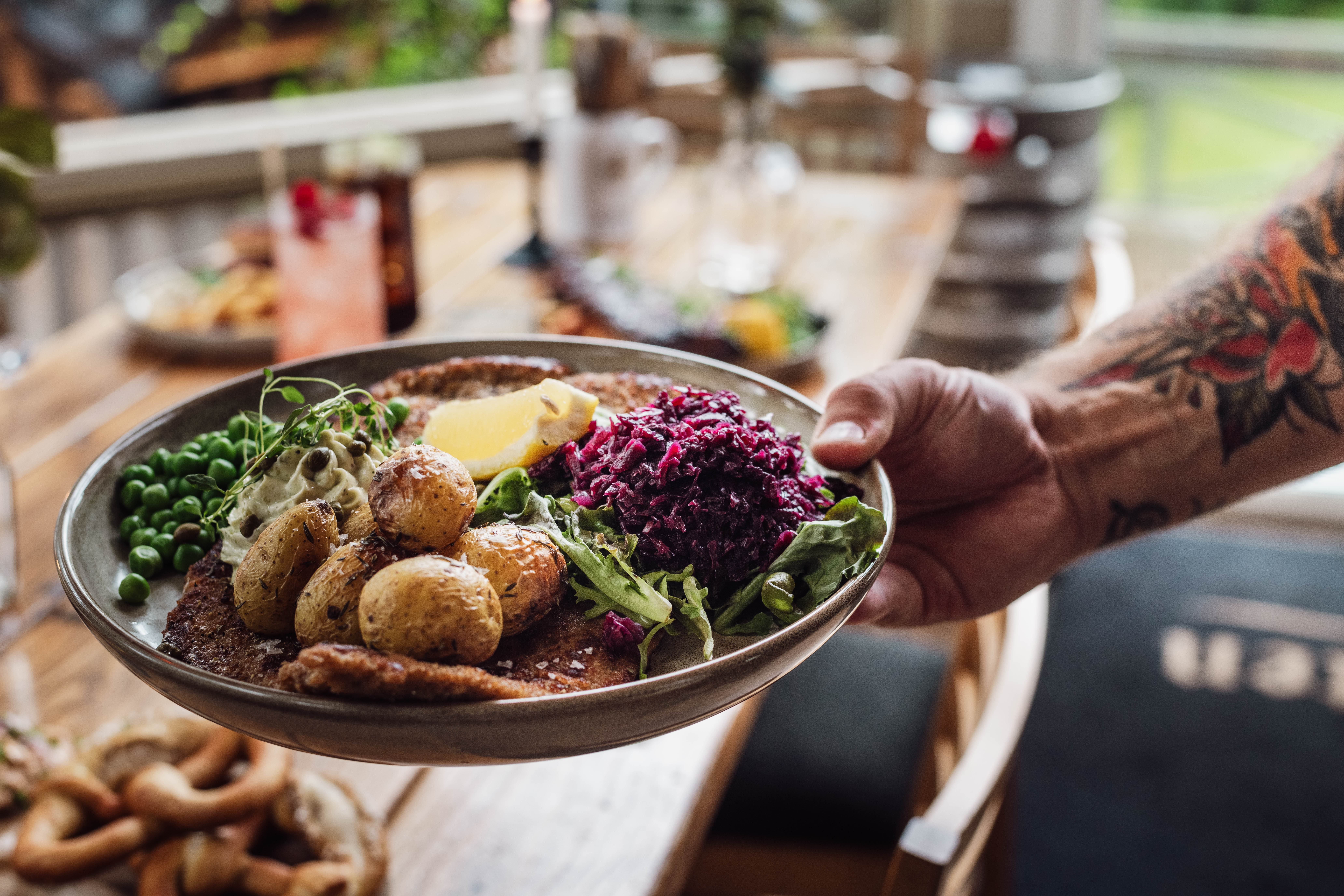 A hand with a tattoo is holding a plate with food. 