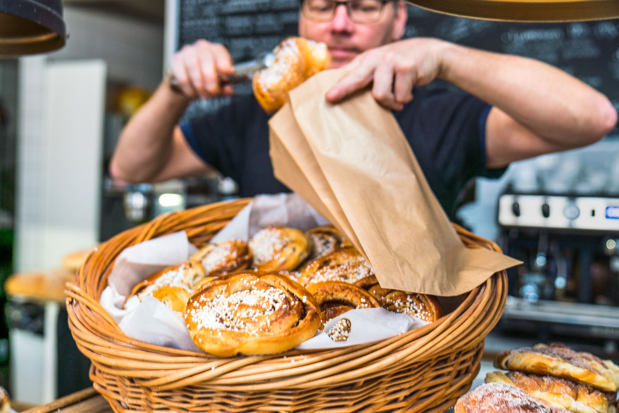 Café owner puts newly baked cinnamon buns in a bag. 