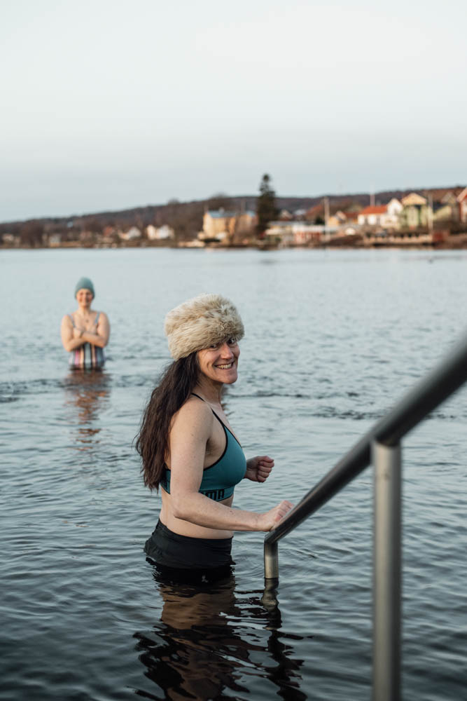 The woman is standing with a winter hat on and going down a ladder into the water. Lots of houses can be seen in the background