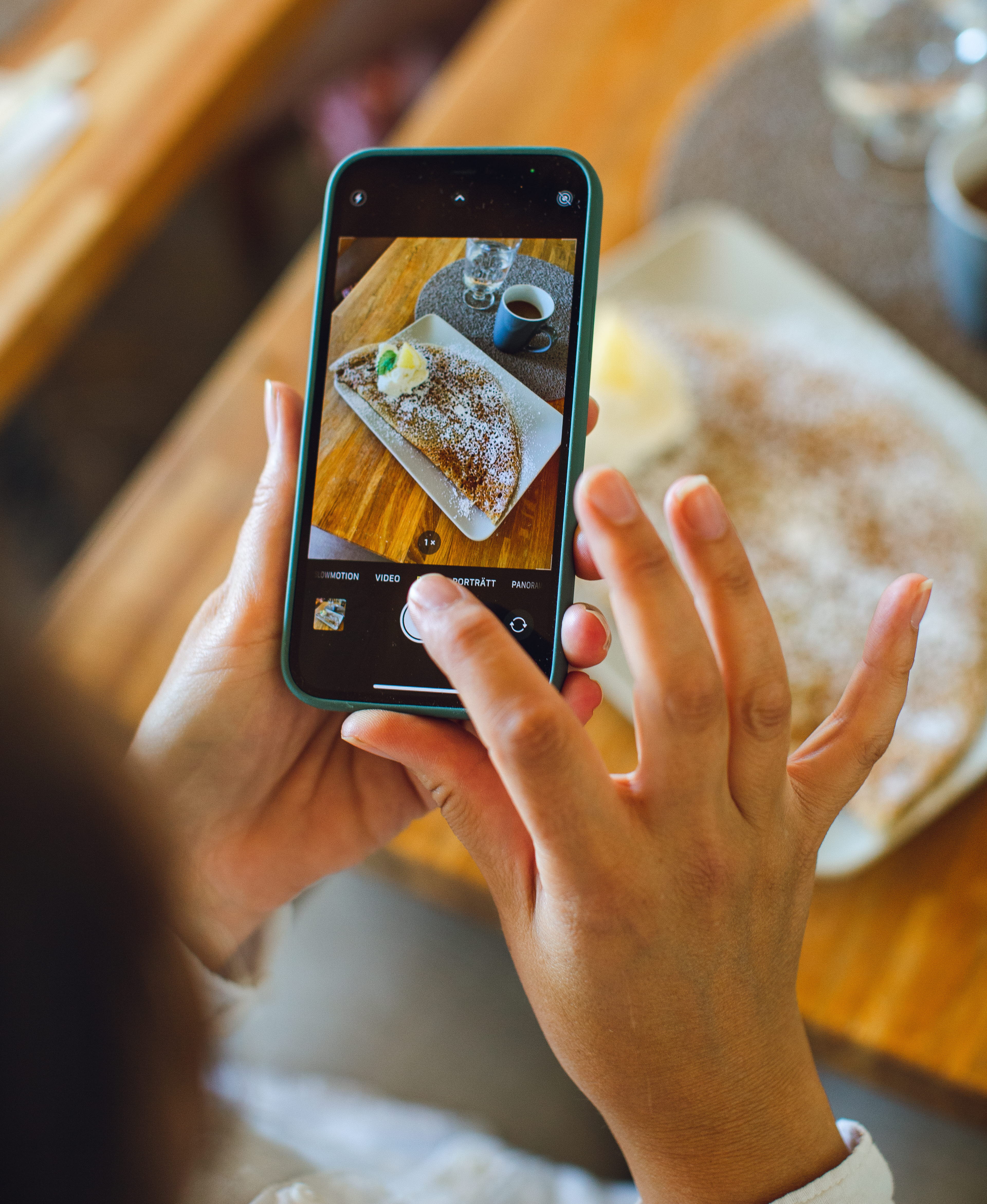 A person is taking a picture with a smartphone. In the phone you can see the picture which is a picture of a crêpe and a cup of coffee.