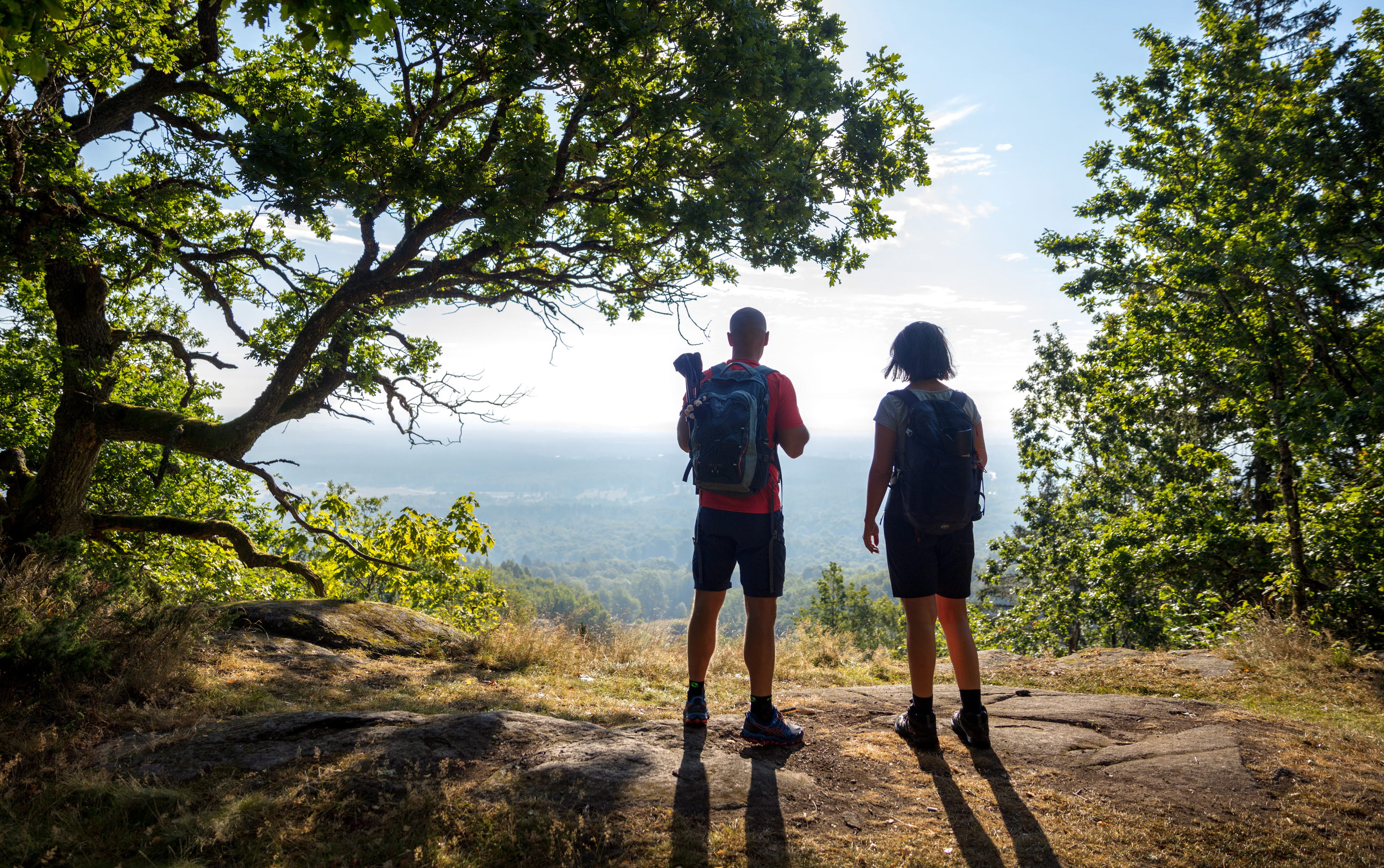 Two people stand on the edge of a mountain looking out over a magnificent landscape