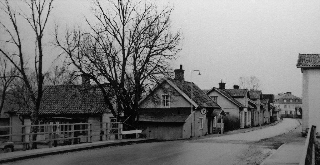 Black and white archive image of a bridge. Beyond the bridge, houses line the road.