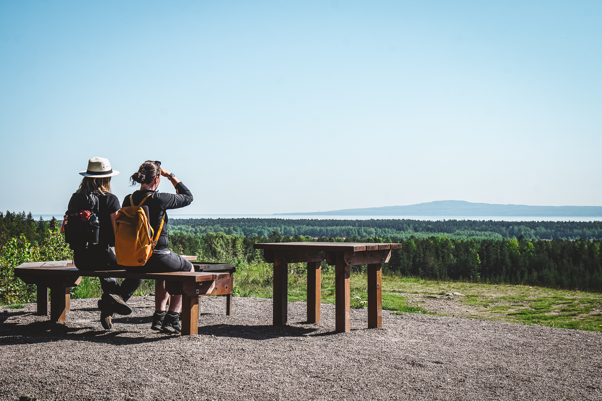 Two women sitting on a bench looking out over the landscape with Kinnekulle at the horizon. 