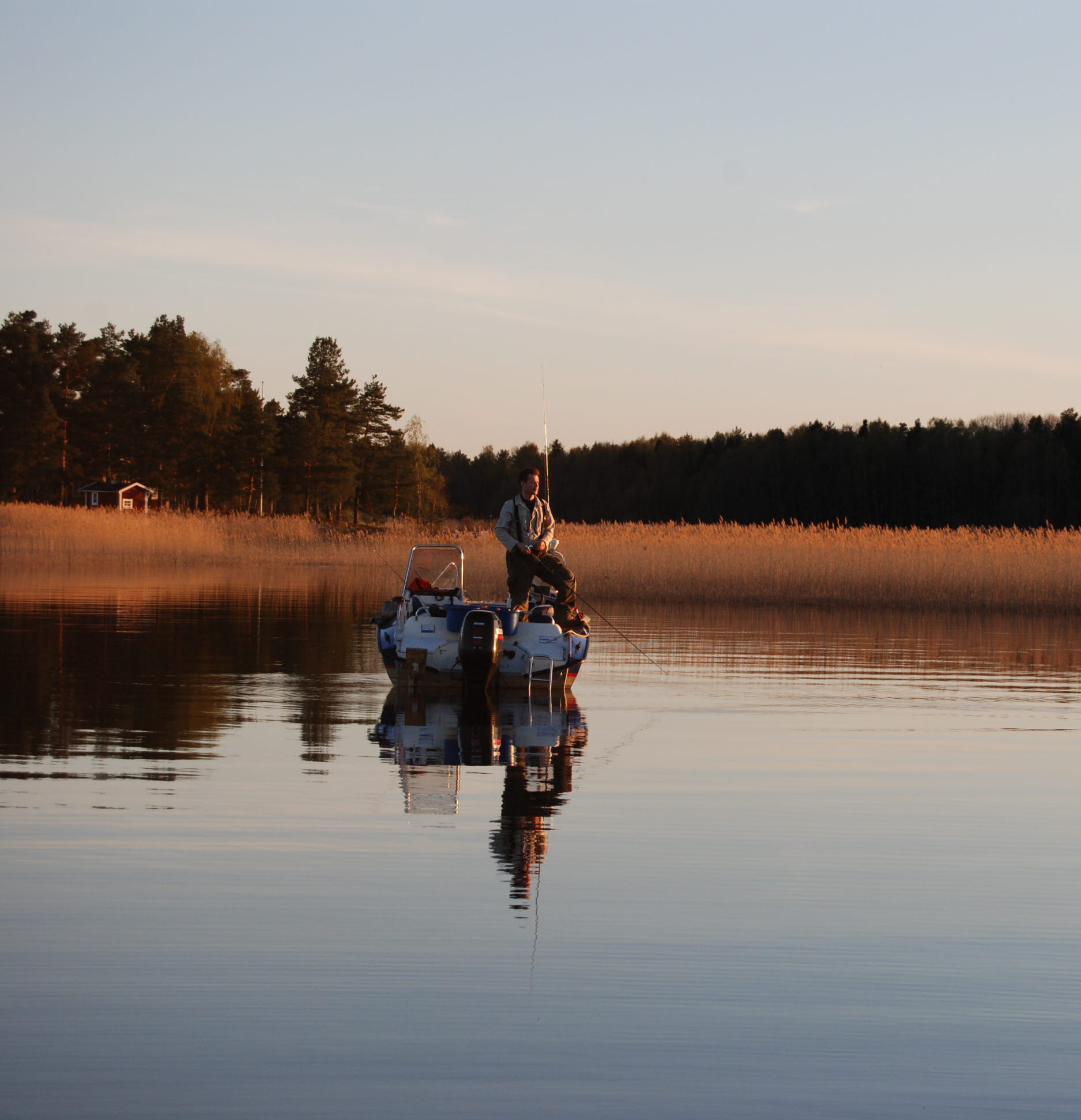 A man is fishing from a boat on a nice summer evening at dusk.