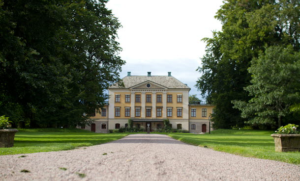 En gul herrgård och en grusgång framför.