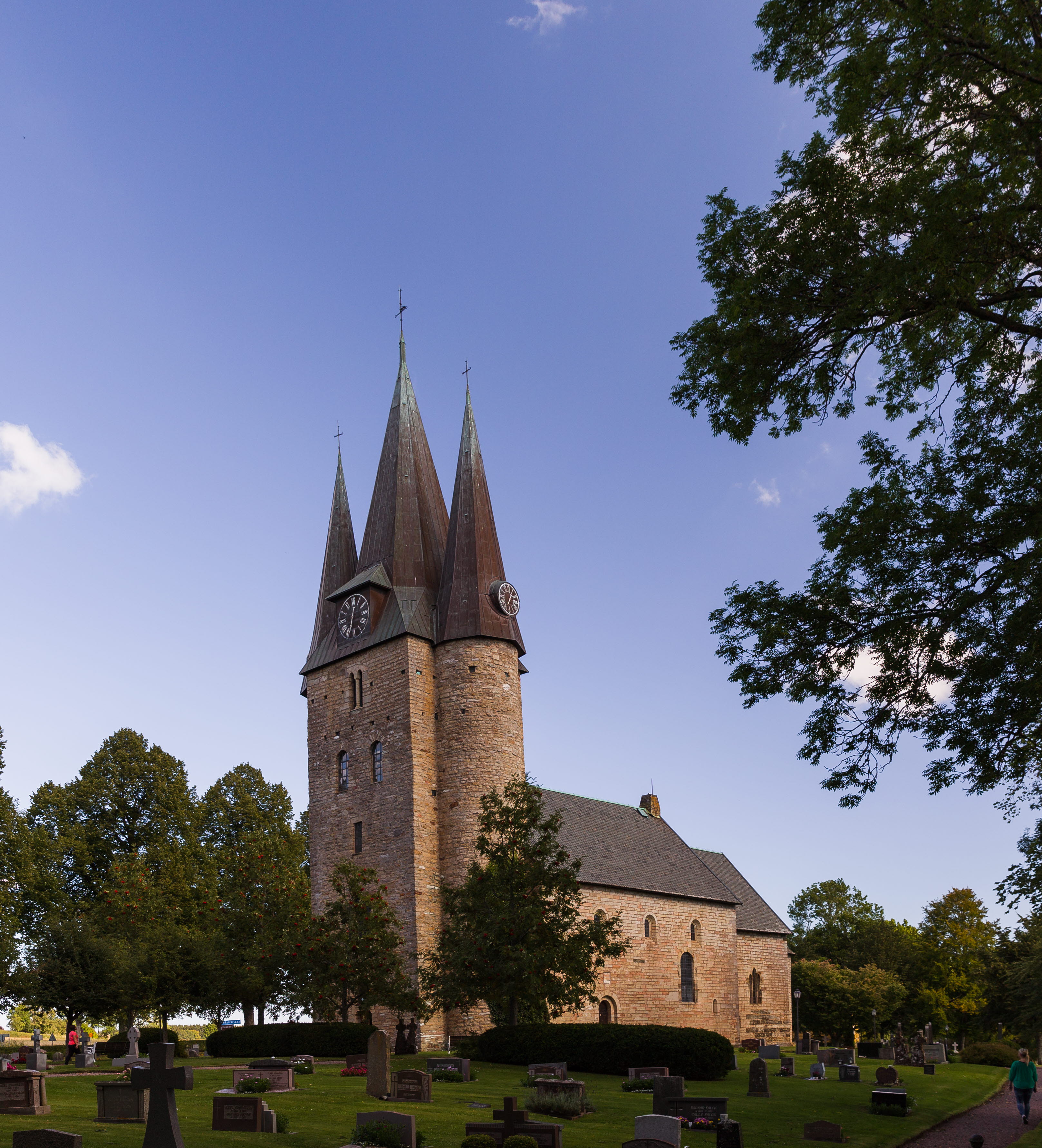 Old church with three towers. In front of the church is a graveyard with gravestones and trees.