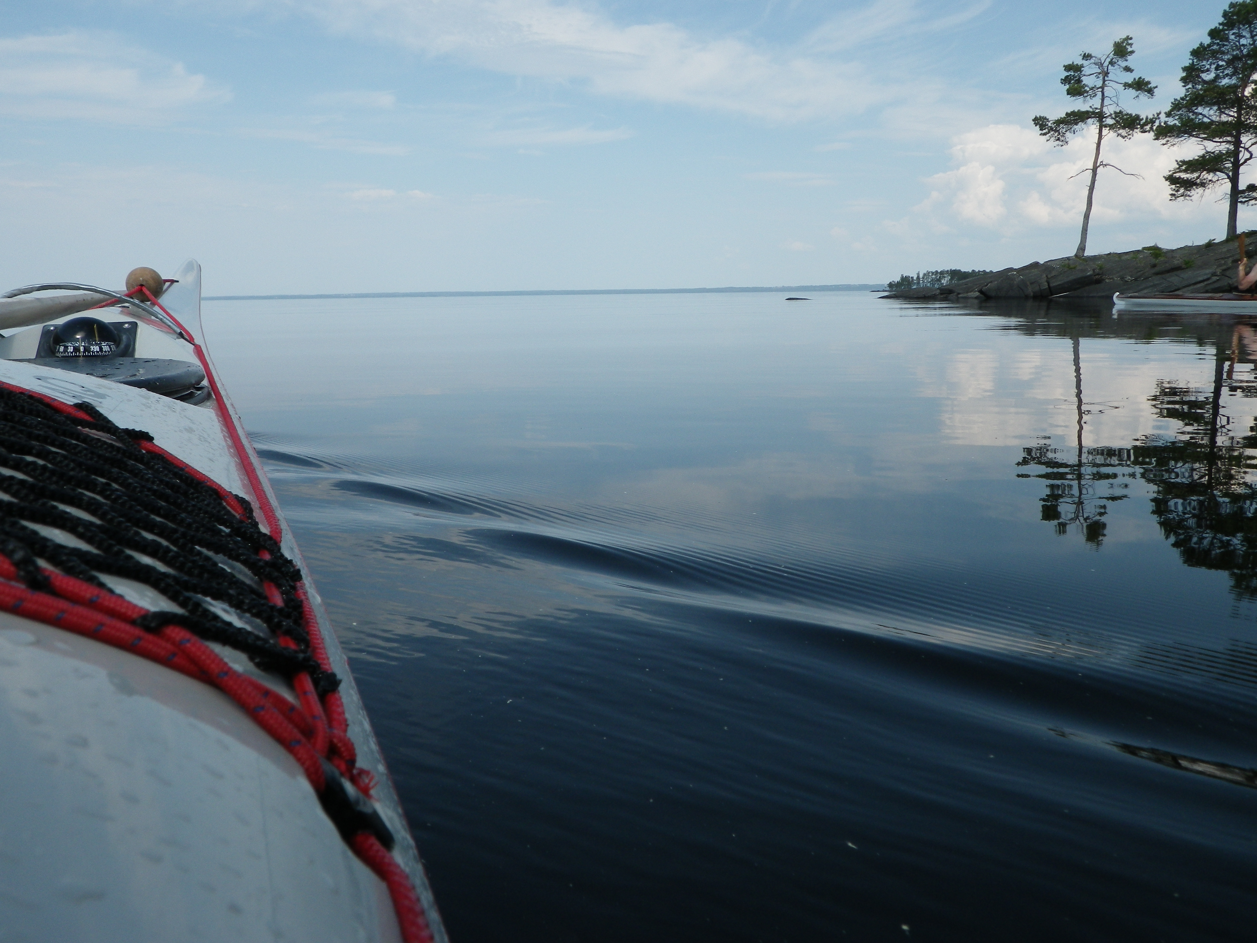 Here we see the top of the kayak gliding through Lake Vänern with a small island on its right side with one alone tree.