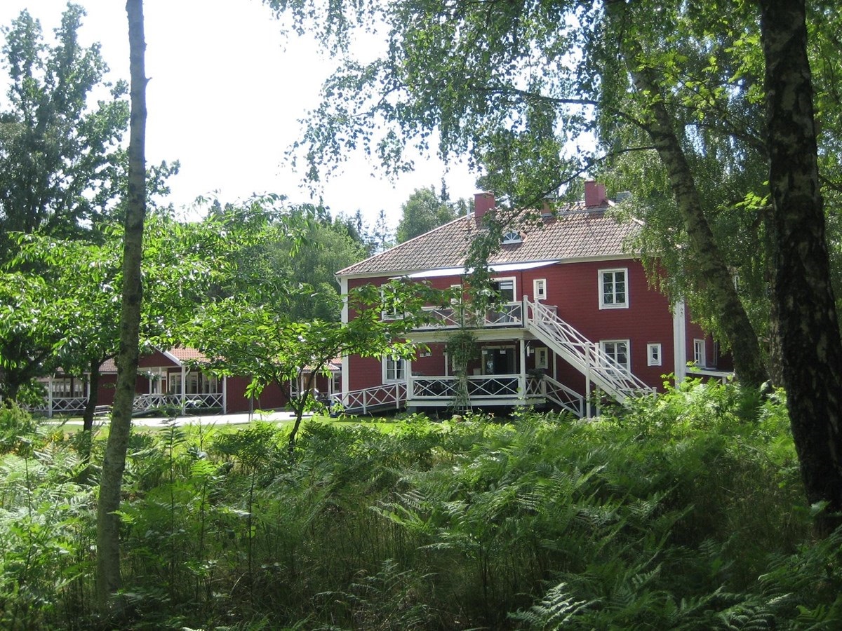 A red larger house with white knots, stairs and porches located in a lush area.