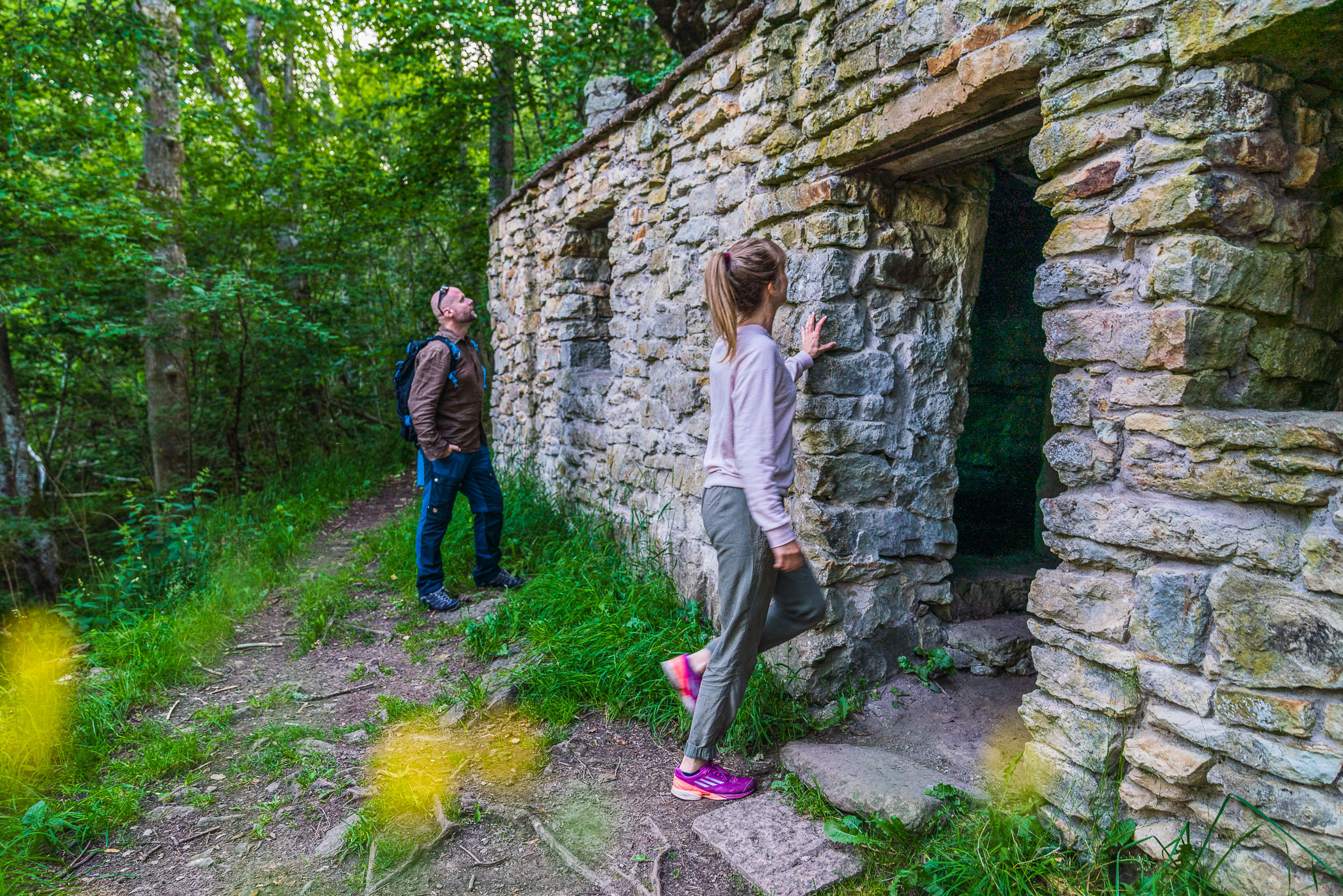 Two people, a man and a woman, view a stone cave in the forest.
