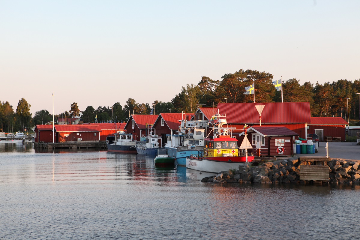 Spikens fishingharbour with a couple of boats along the wharf. Small fishing huts in the background. The evening sun is shining low and the water is still.
