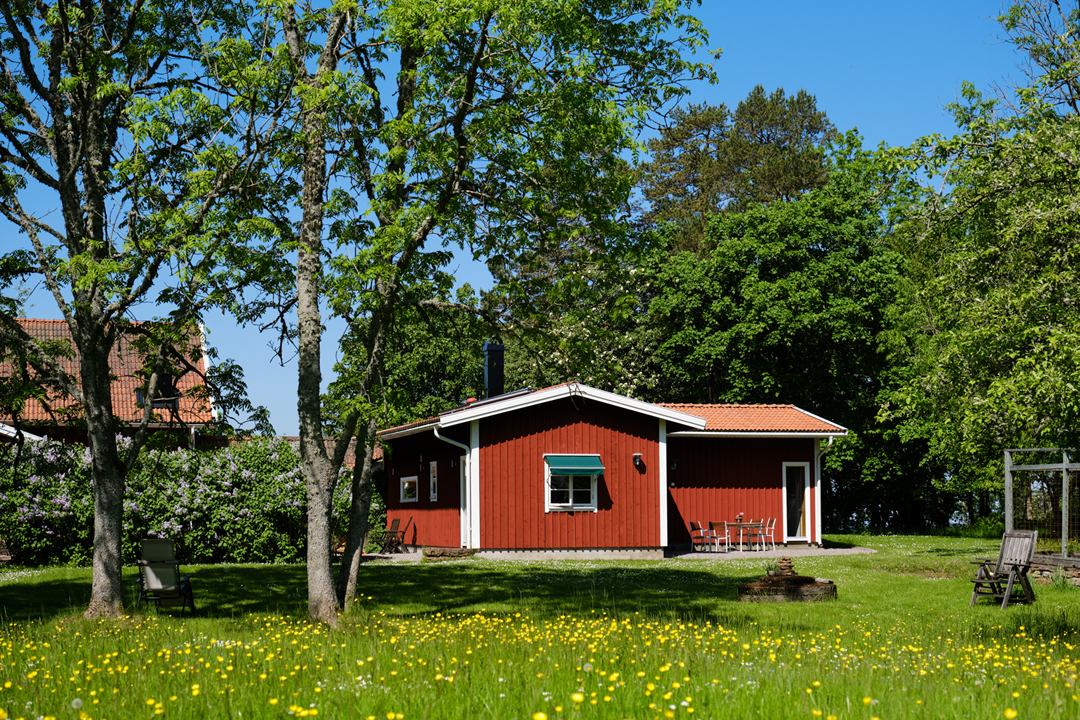 A red cottage with green grass and green trees can be seen .