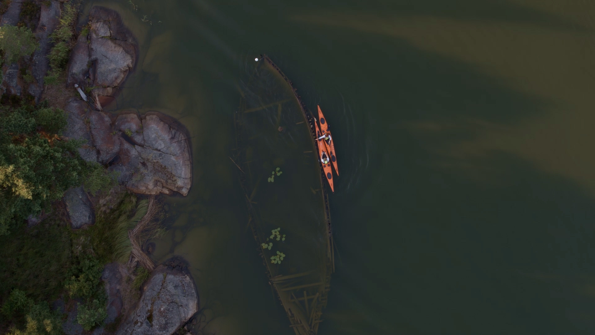 An overview of a ship wreck lying visible in a lake with a kayak on the side.