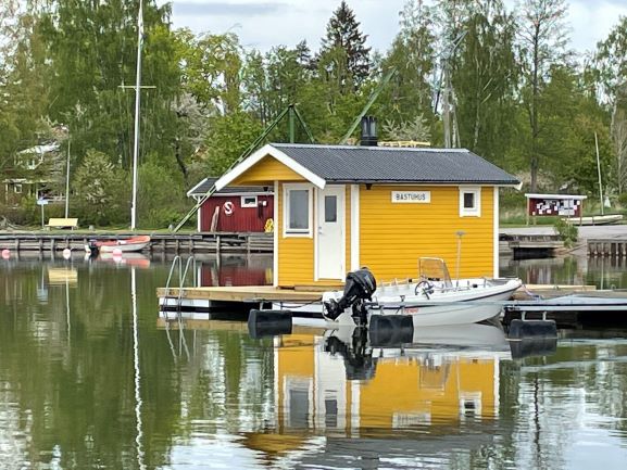 A small, yellow sauna house on a jetty in a harbour. A small motorboat in the foreground.