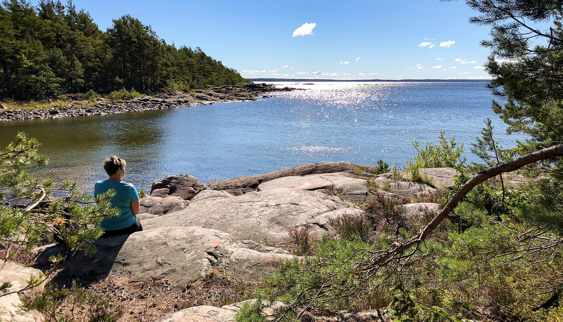 A woman is sitting on a cliff and looking out over the water.