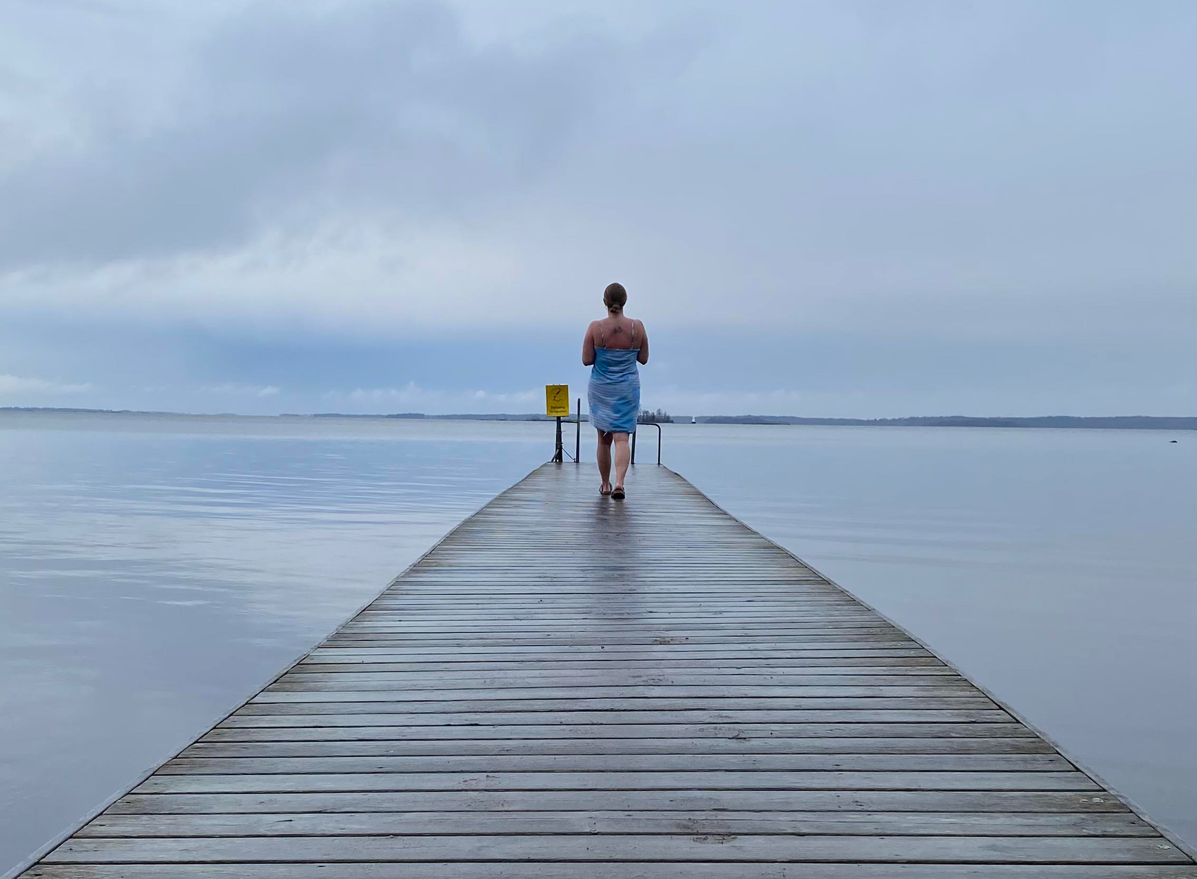 A person walking on a jetty with a towel wrapped around the body.