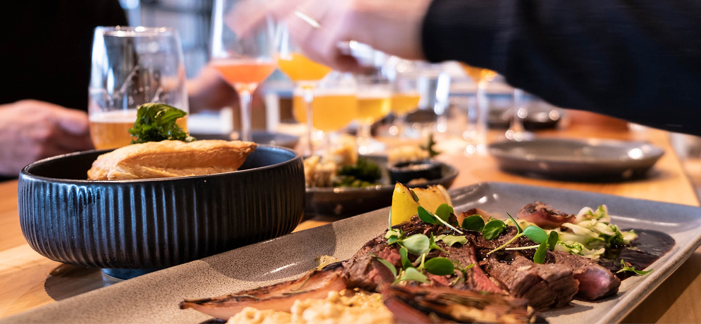 A plate with a dish consisting of meat and potatoes laid out on a beautiful plate and for this beer is served in a glass.