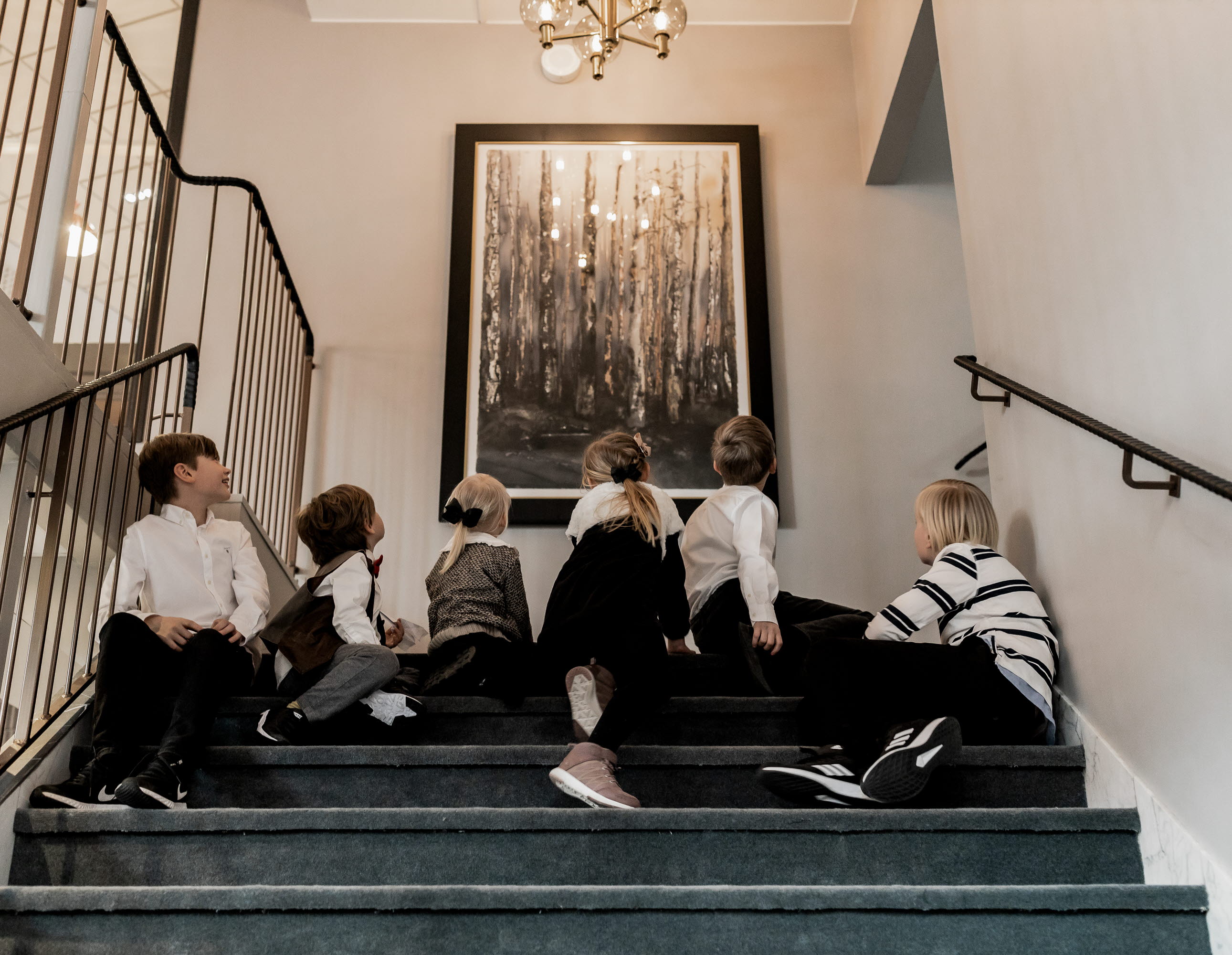 Six kids are sitting in a staircase looking at a large painting.
