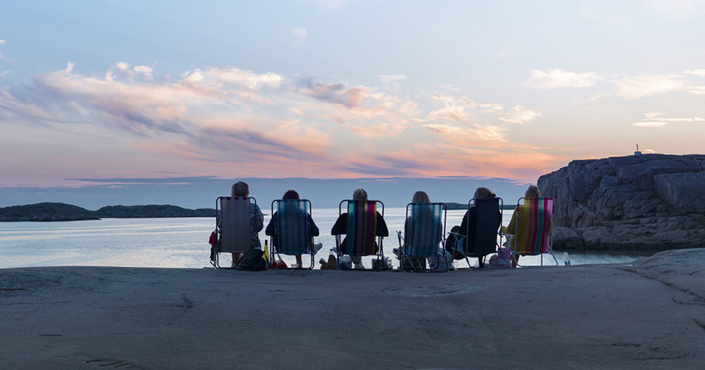 Overview image of Skövde with lots of rooftops and greenery. The pink sunset lights up the sky behind the mountain Billingen.