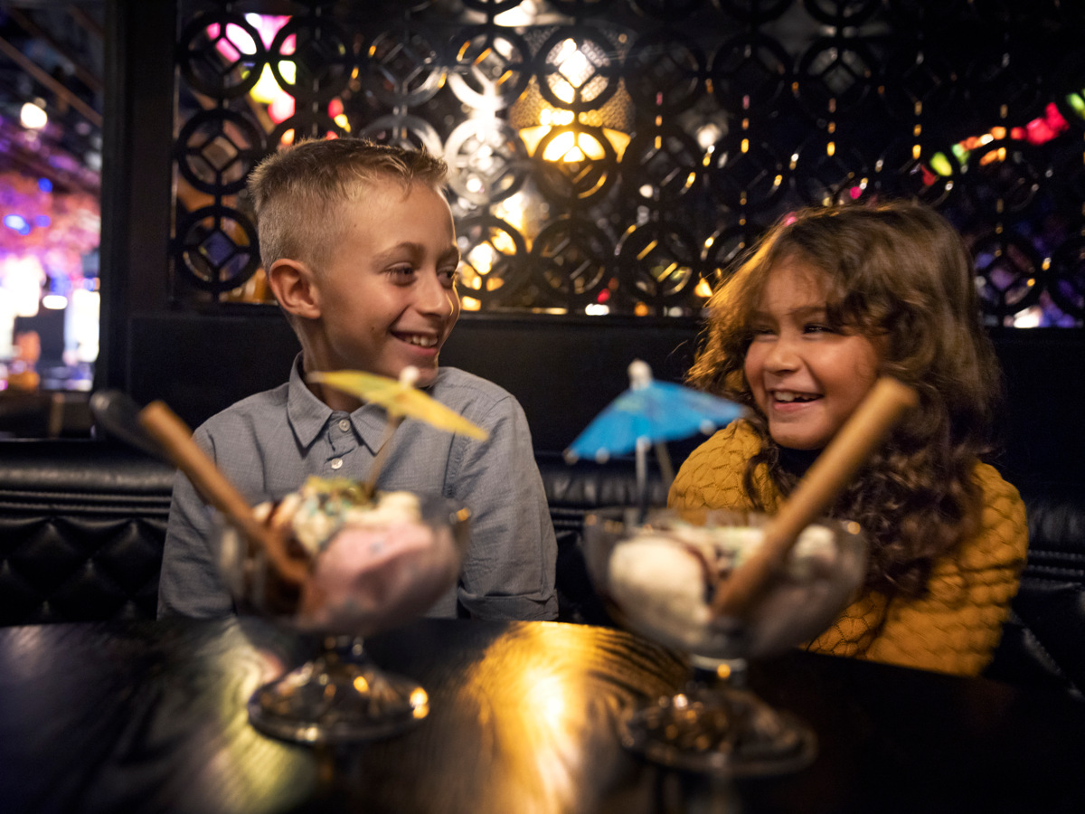 A boy and a girl sittning in a restaurant with two desserts in front of them. 