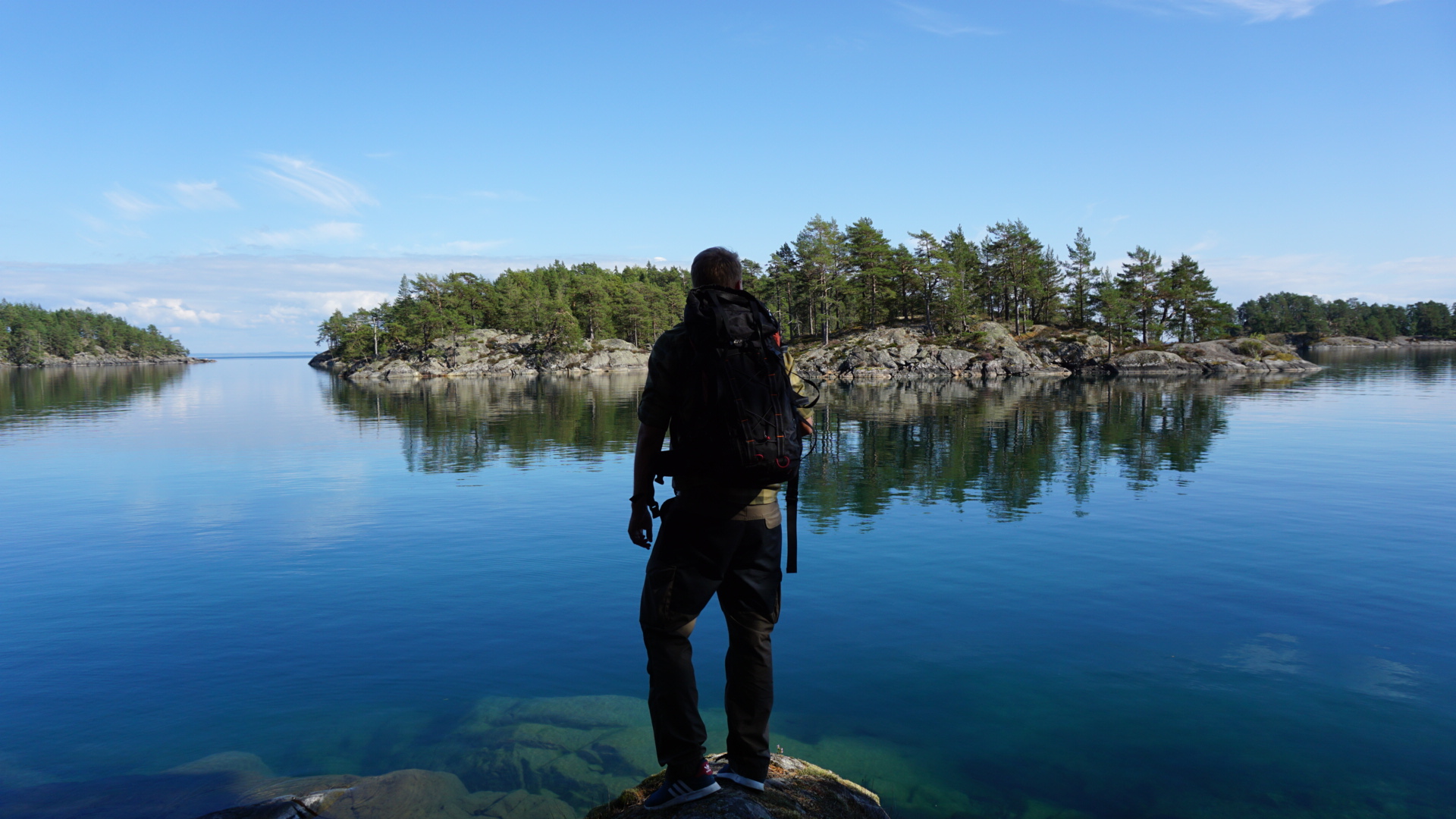 The silhouette of a man standing on the edge of a cliff gazing out over the clear blue water.