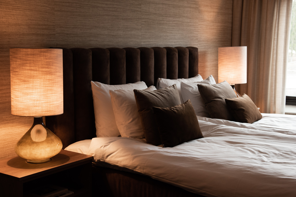 A hotel bed made with large lamps on the bedside tables, all in 70s style with brown and light tones.