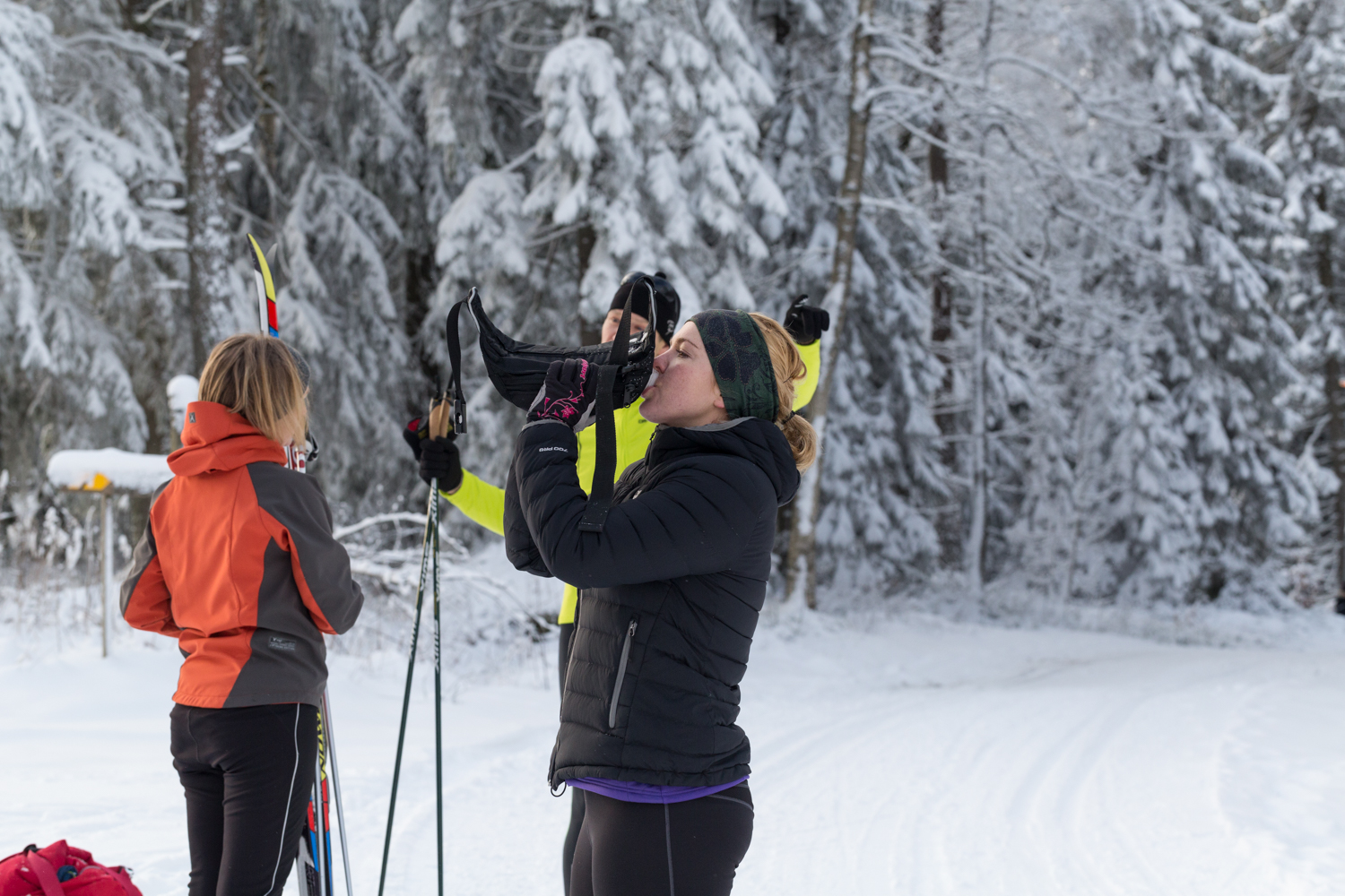 Three persons on cross country skiis are taking a break drinking water. 