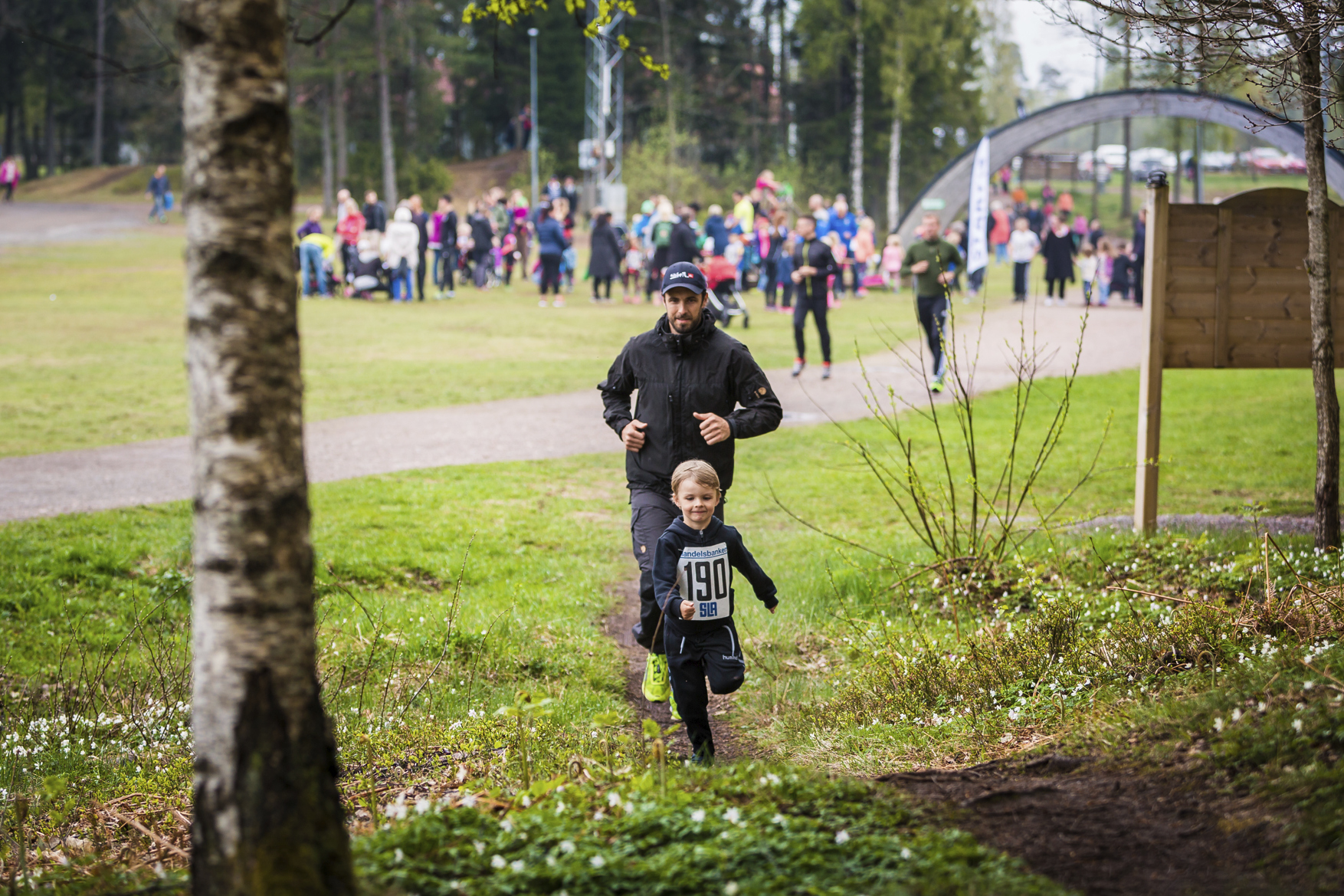 Ett barn med nummerlapp springer i skogen med sin pappa. 