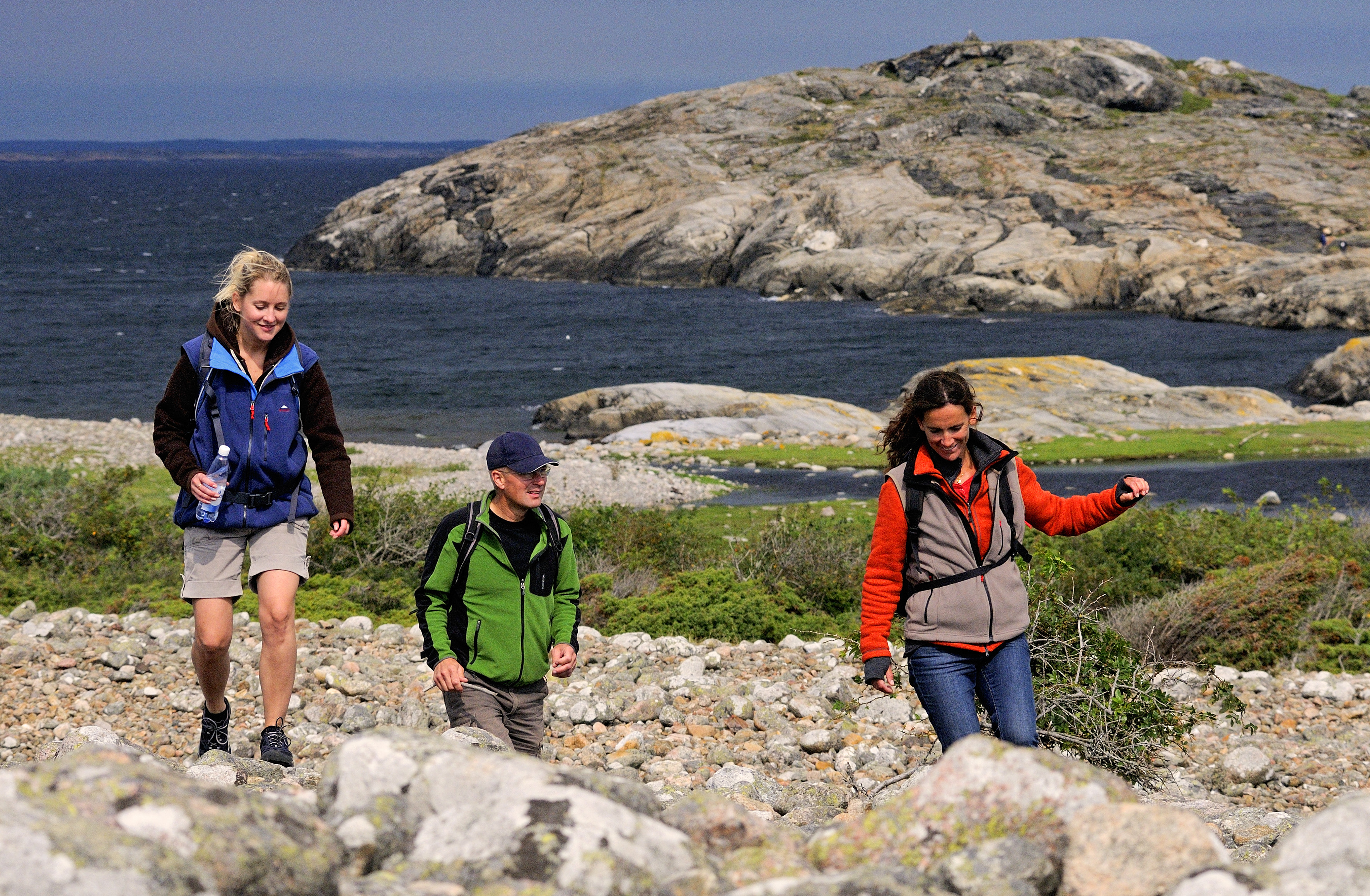 Three people are hiking across a cobblestone field at North Koster.